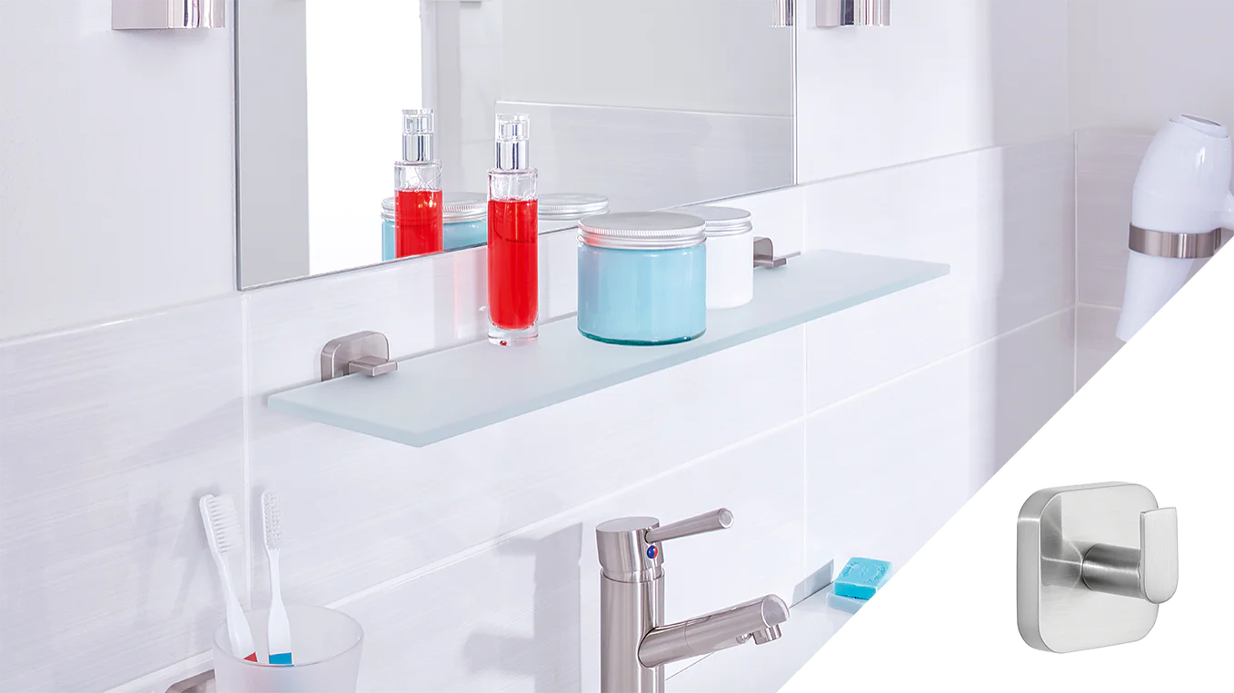 A modern bathroom counter with a glass shelf holding two bottles and a jar, one red and one blue. A mirror is above the shelf. Toothbrushes and a soap dispenser are on the counter. A small metallic wall hook, secured with tesa tape, is shown in a separate inset. (This text has been generated by AI)