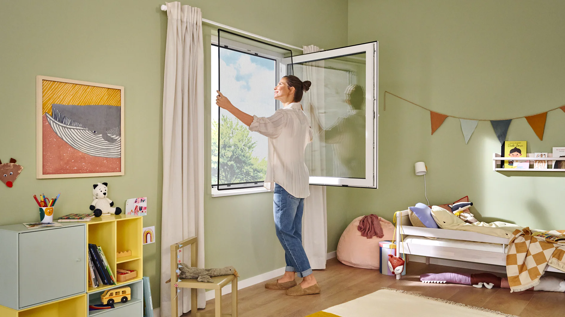 A woman opens a window in a childs room, which has green walls and wooden flooring. The room features a bed, a shelving unit with books and toys, a chair, and a wall decorated with bunting hung using tesa tape. Sunlight streams in, brightening the space. (This text has been generated by AI)