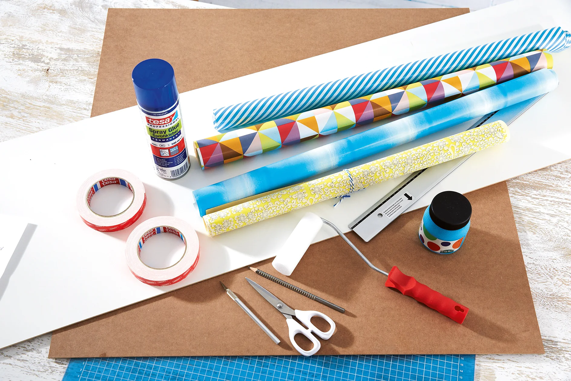 Shelves of different sizes, preferably with square compartments, 3 mm deep MDF panels (cut to the size of the shelf backs), a 3 mm HDF panel painted white on one side (for the blackboard, cut to the size of the shelf side), chalkboard paint, a paint roller, scissors, utility knife, pencil, ruler, decorative paper, alcohol- or silicone-free glass cleaner, tesa® Spray Glue PERMANENT, tesa Powerbond® ULTRA STRONG 5 m x 19 mm (2 rolls)