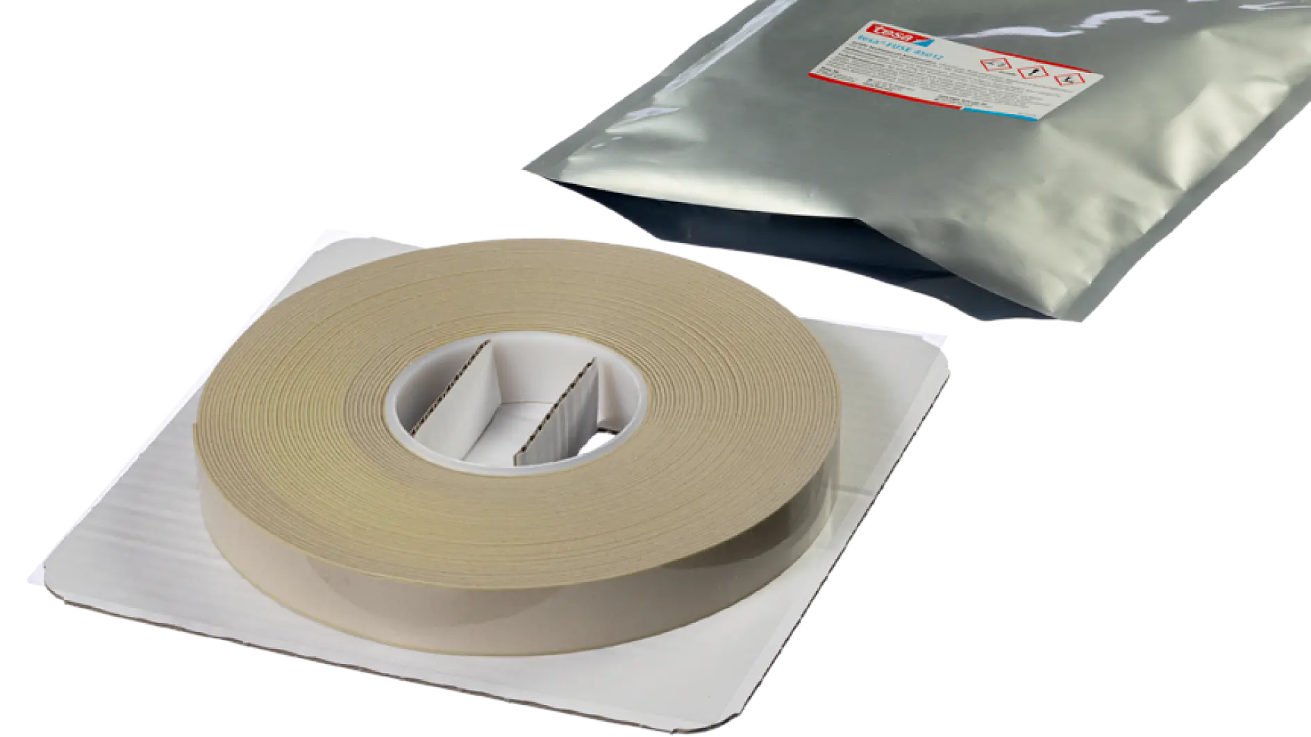 A large roll of beige tesa tape is placed on a white cardboard holder. Behind it, there is a silver-colored foil package with a label. The scene appears to be set on a plain white background.