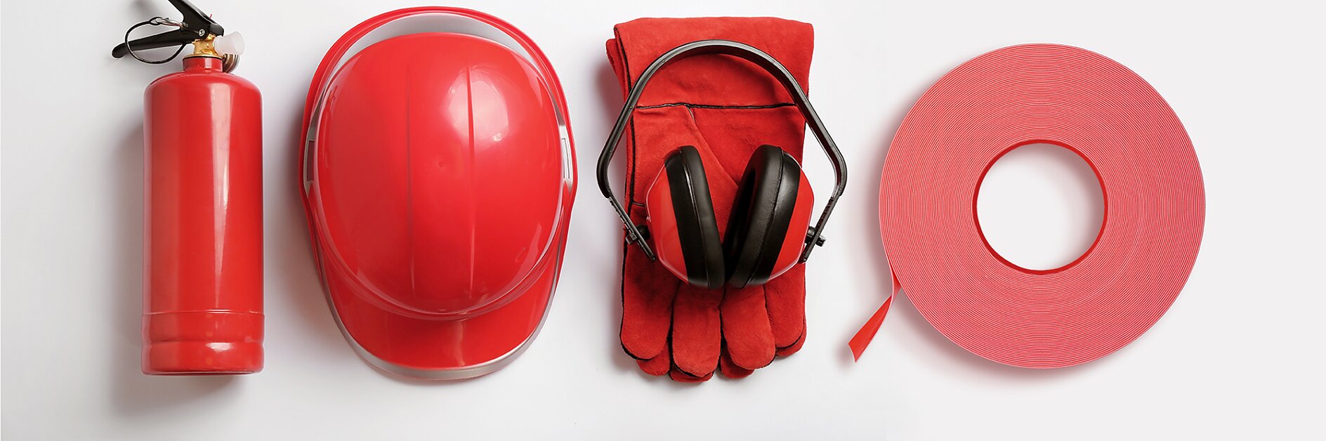 A red fire extinguisher, a red hard hat, black earmuffs placed on red gloves, and a red rolled fire hose are lined up against a white background.