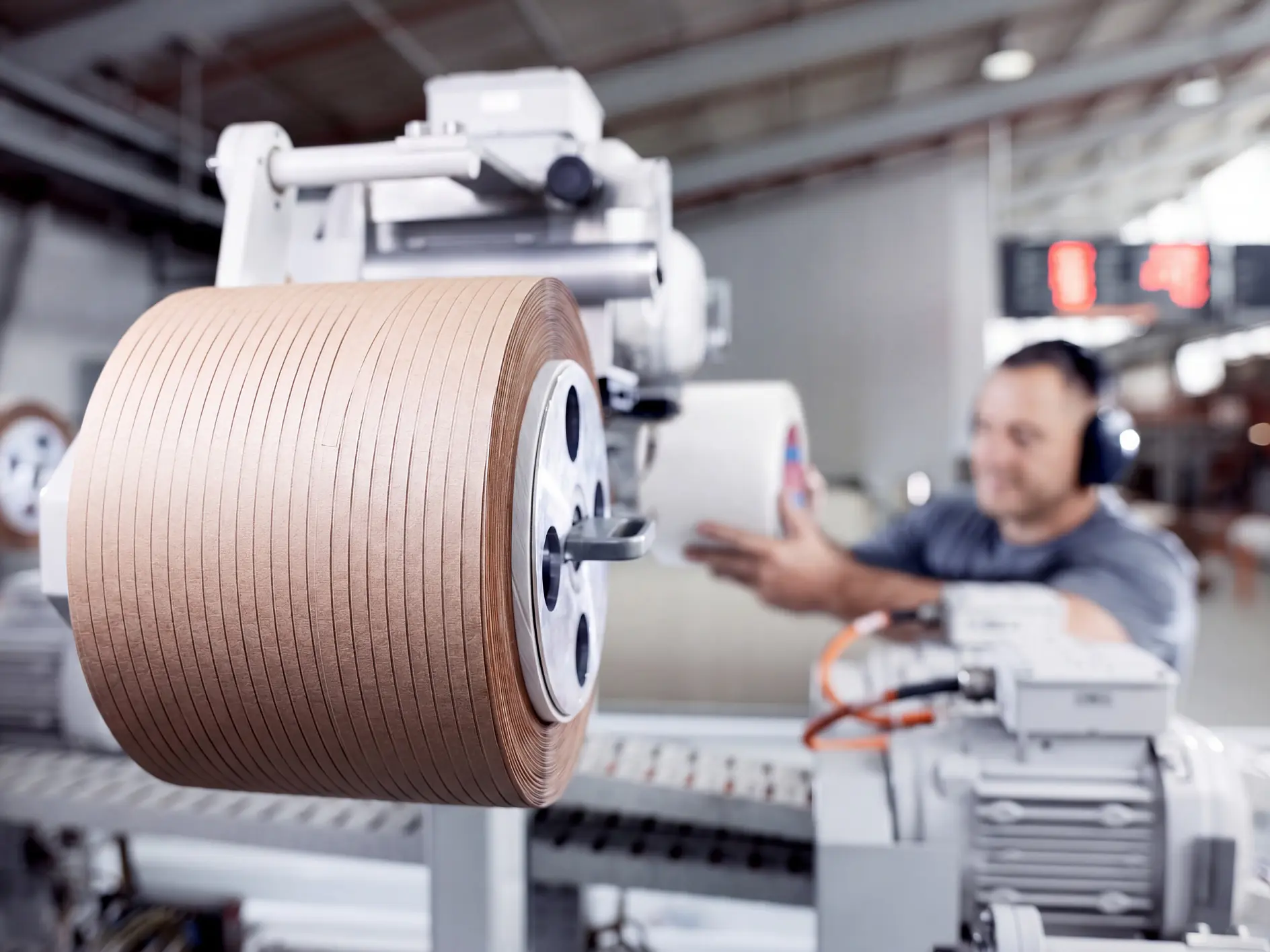 Ruban adhésif brun industriel marqué tesa enroulé sur une machine dans un environnement d'usine, avec un ouvrier opérant les commandes à proximité