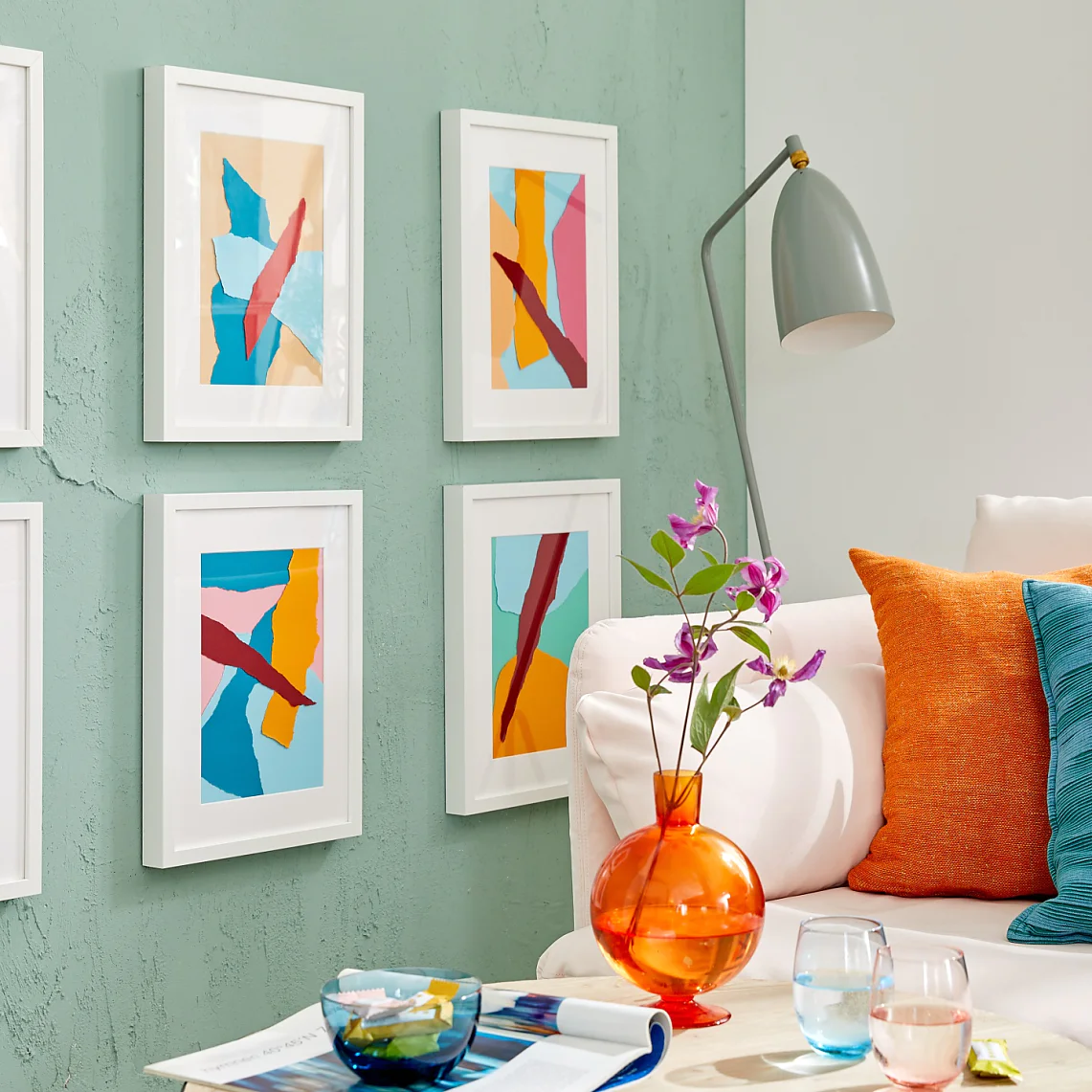 Magyar fordítás: Egy pasztellzöld falú szobában hat színes, absztrakt műalkotás látható fehér keretekben. Alatta fehér kanapé kék és narancssárga párnákkal. A falon szürke lámpa van, a kis asztalon pedig egy váza lila virágokkal és néhány pohár; mindet tesa ragasztószalag rögzíti. (This text has been generated by AI)