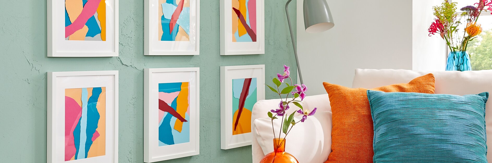 Magyar fordítás: Egy pasztellzöld falú szobában hat színes, absztrakt műalkotás látható fehér keretekben. Alatta fehér kanapé kék és narancssárga párnákkal. A falon szürke lámpa van, a kis asztalon pedig egy váza lila virágokkal és néhány pohár; mindet tesa ragasztószalag rögzíti. (This text has been generated by AI)