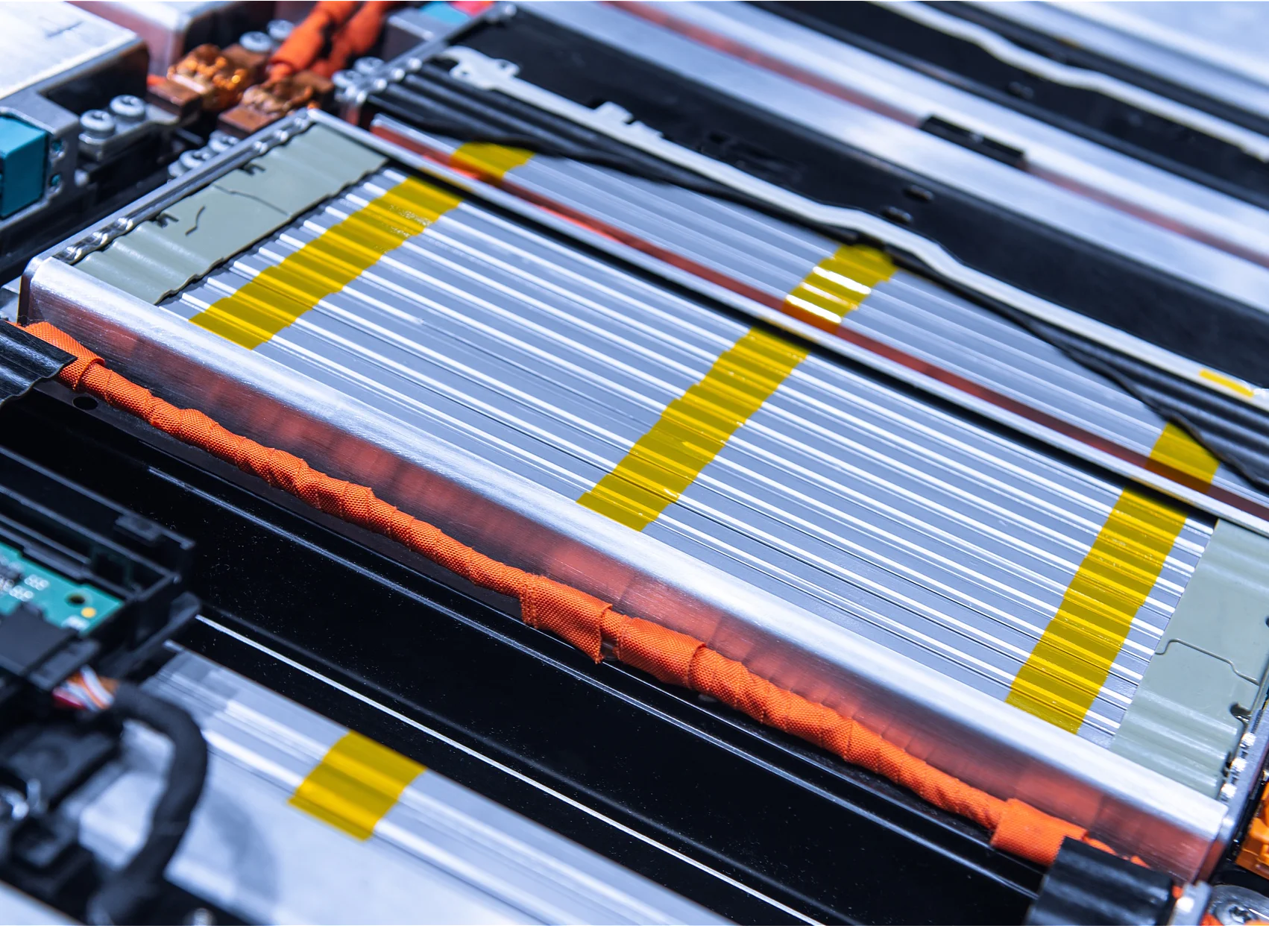 Close-up of a complex electrical circuit board and battery pack, featuring silver and yellow striped battery cells, orange wires, and a green circuit board. The components are tightly arranged within a metallic frame using tesa tape. (This text has been generated by AI)