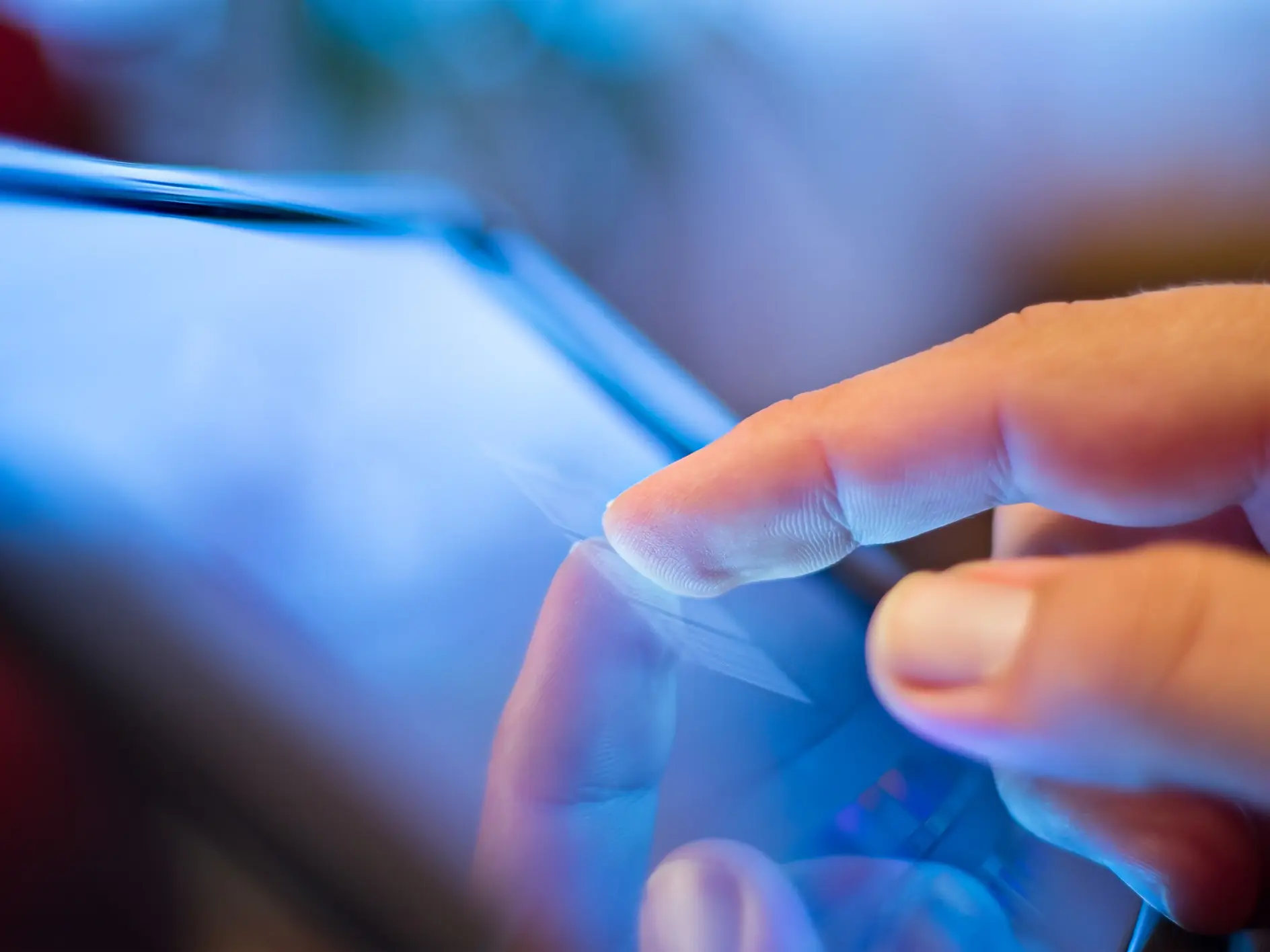 Hand touching a tablet screen indoors, reflecting finger on the glass surface, highlighting touchscreen interaction technology.
