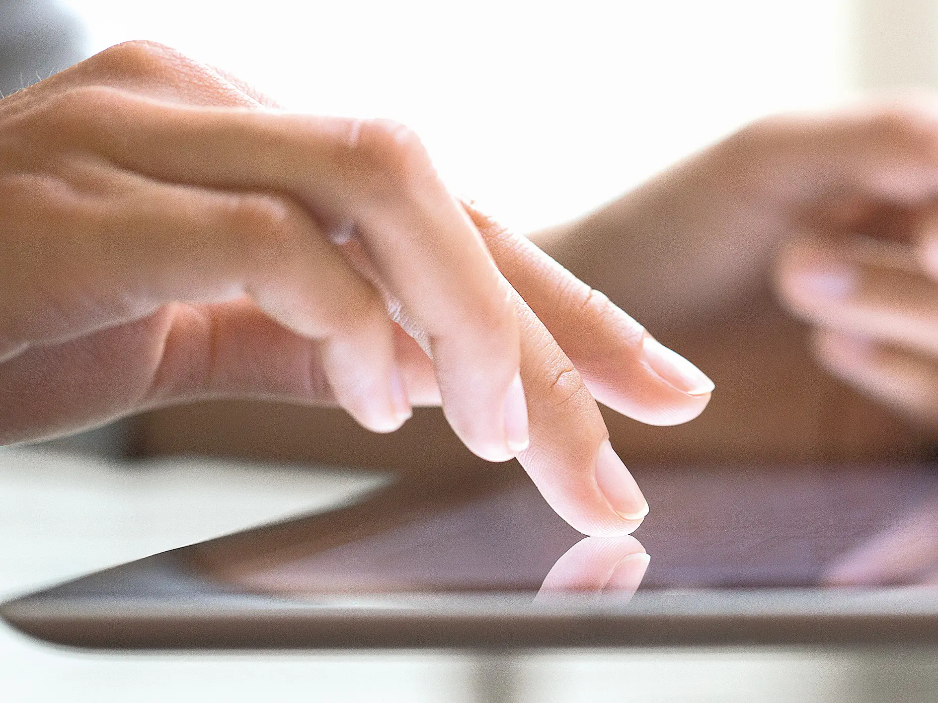 Close-up of a persons hands using a tablet. One hand is touching the screen while the other holds the device securely with tesa tape. The background is softly blurred, highlighting the focus on the interaction with the touchscreen.