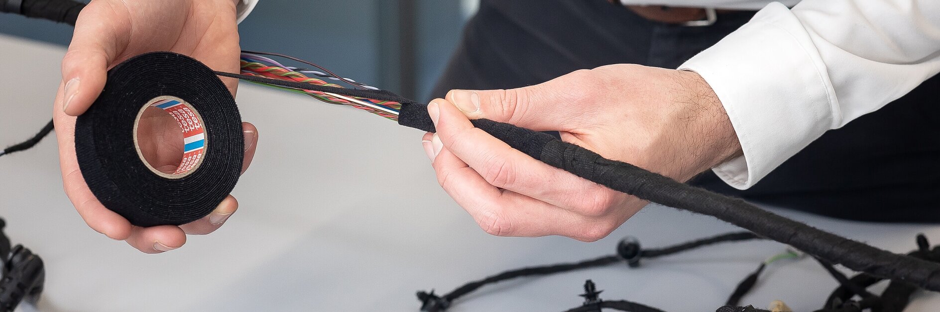 tesa tape being applied to an automotive wiring harness on a white table in an indoor workshop setting
