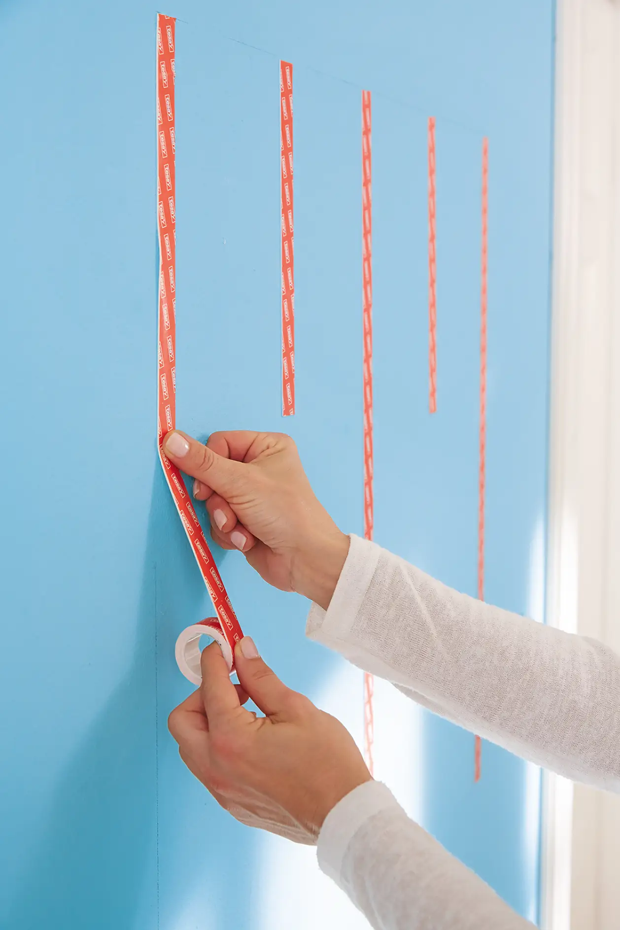 Alternately attach five tesa Powerbond® ULTRA STRONG strips – in full length and in approx. 20 cm strips – vertically on the wall.