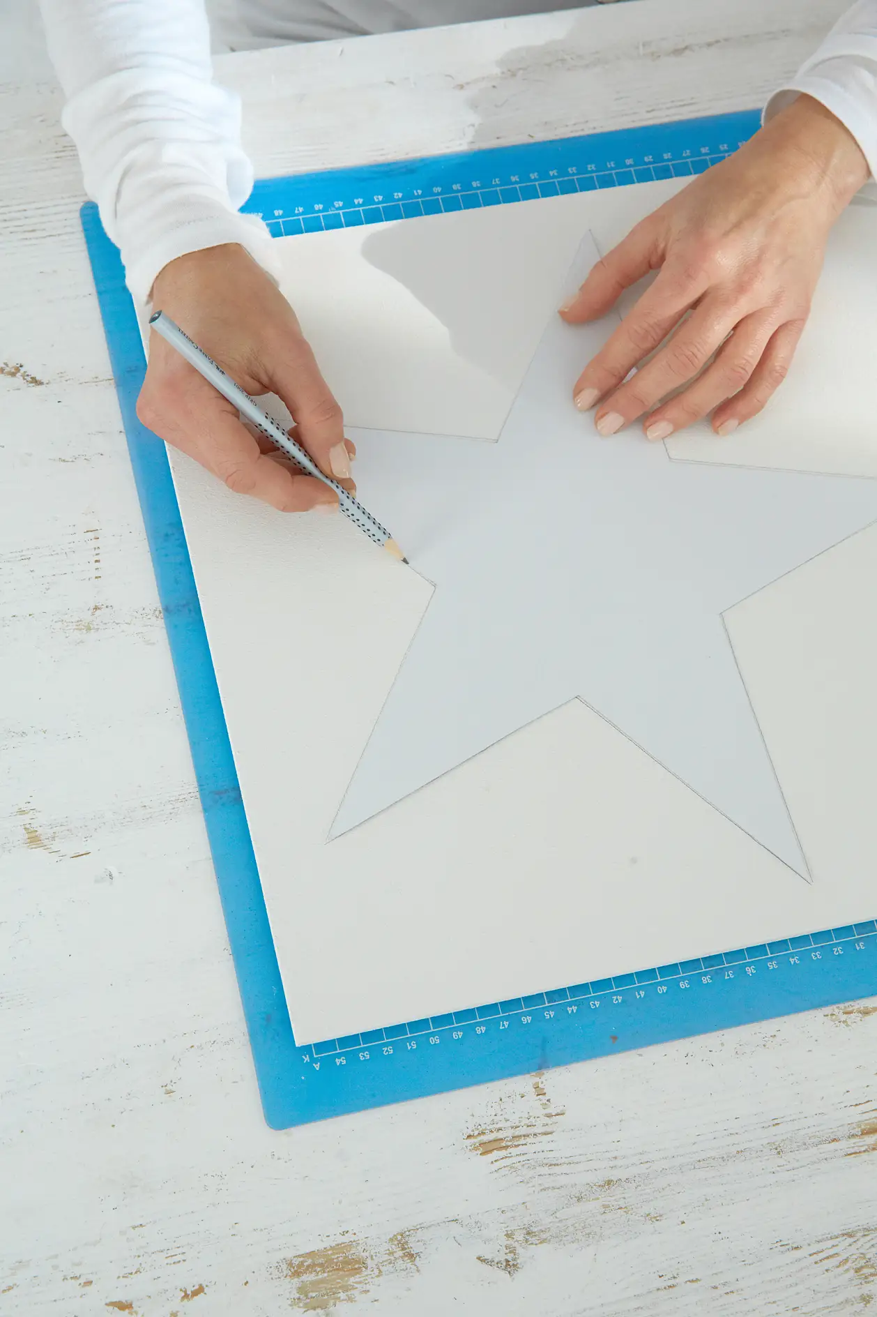 Aus dem festen Papier eine Schablone nach der Vorlage anfertigen. Die Holzplatte mit der weißen Farbe grundieren und den Stern mithilfe der Schablone ca. 3 cm über der unteren schmalen Kante aufzeichnen.
