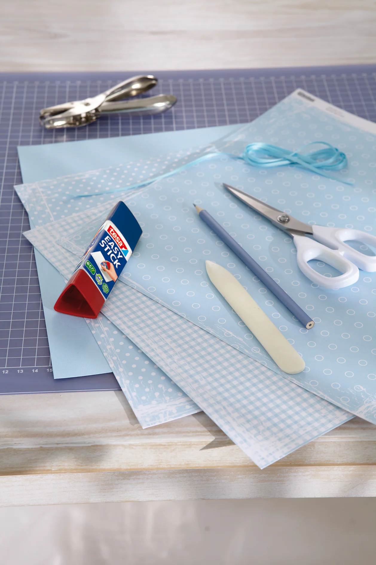Scrapbooking-Papiere mit unterschiedlichen Mustern, Schere, Bleistift, stabiles Papier für die Schablone, Lochzange, Falzbein, Bändchen zum Aufhängen, tesa Easy Stick ecoLogo®.
