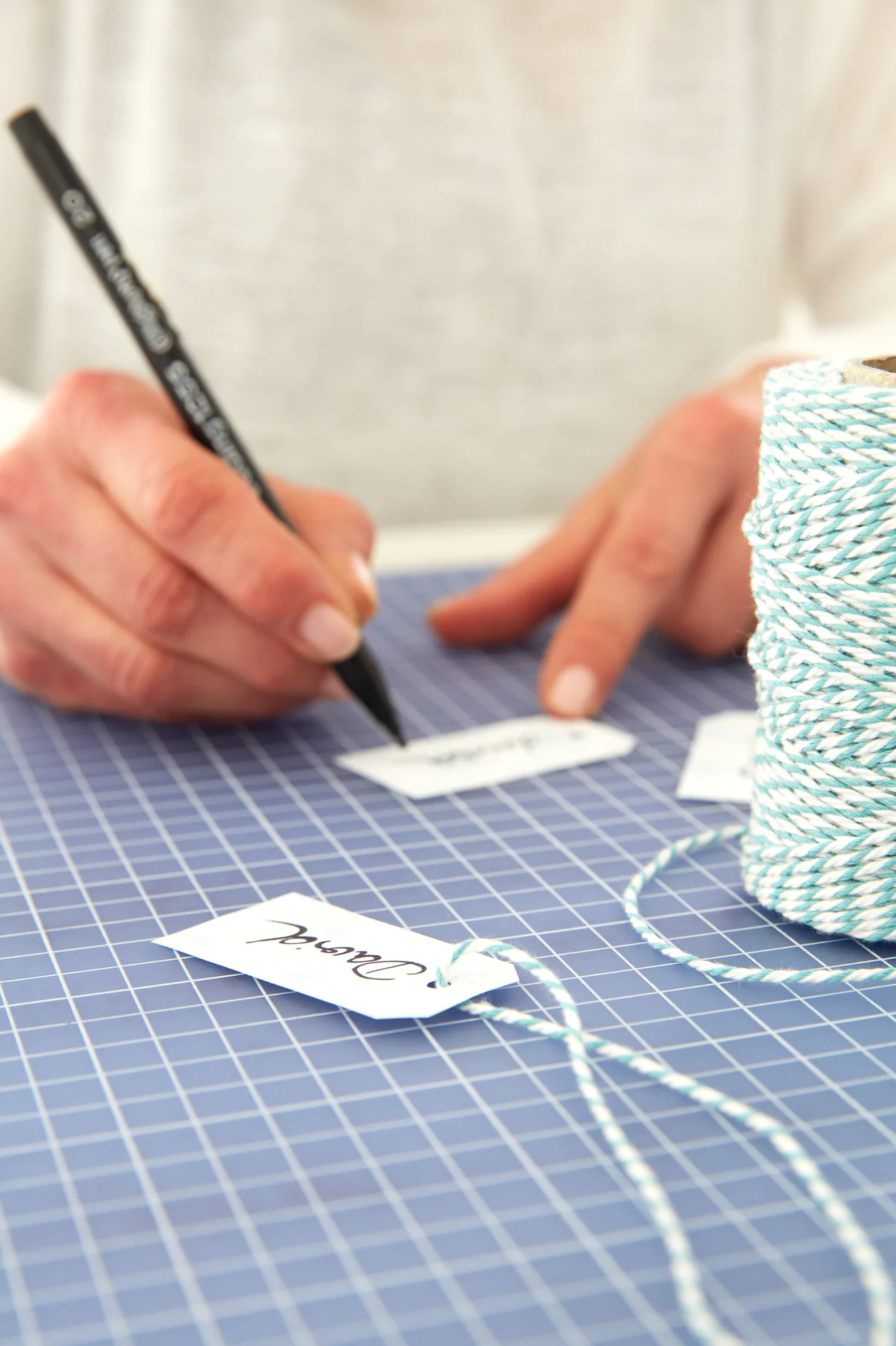 Cut small labels from the remaining paper, write names on them using the calligraphy pen, punch a hole on the upper side and attach the labels to the pouch using the string.