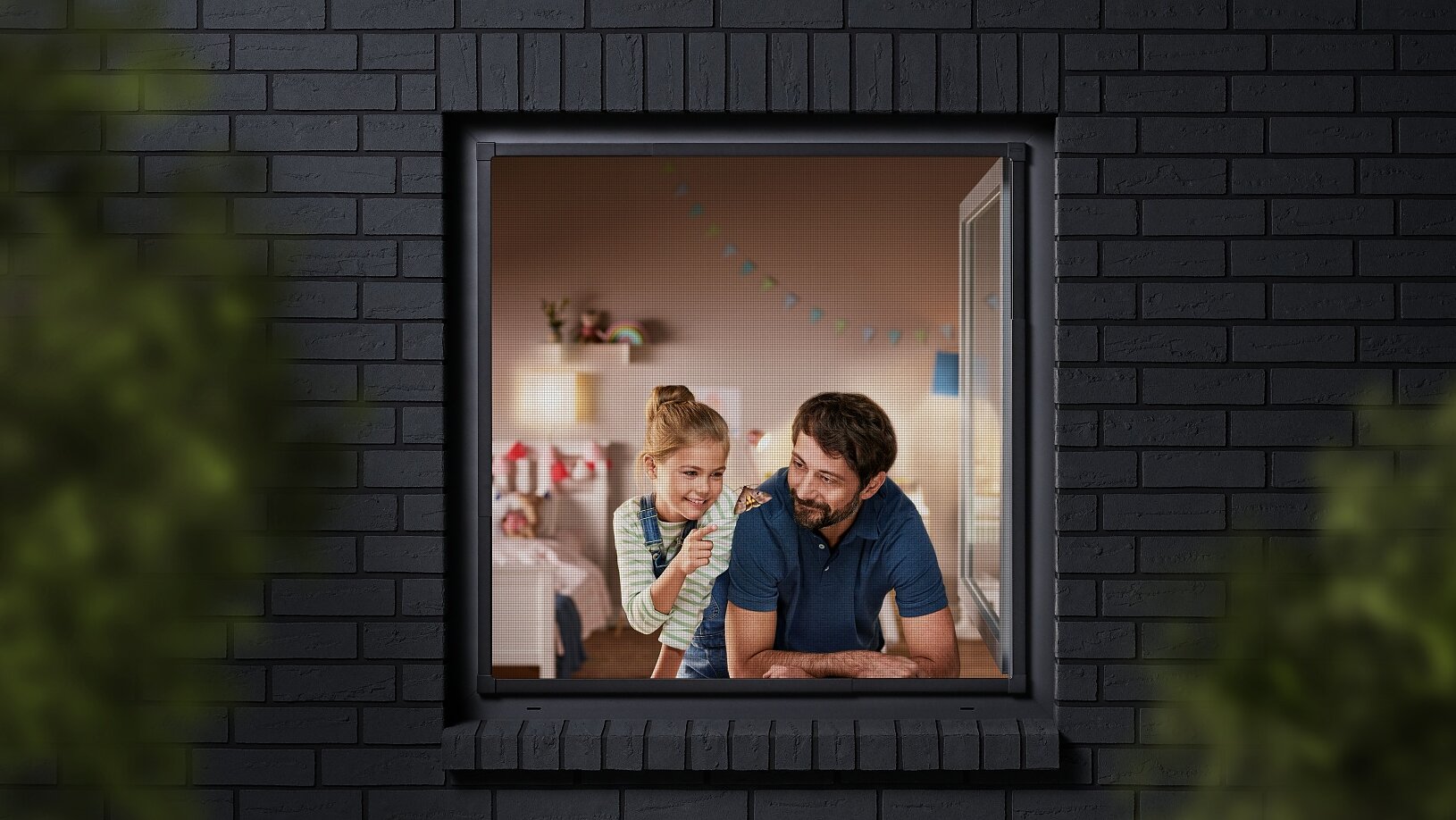 A man and a child are seen through a window, looking into a room decorated with colorful bunting. The building has dark brick walls, and the view is partially framed by blurred greenery. The man is wearing a blue shirt, and the child is sitting beside him. (This text has been generated by AI)