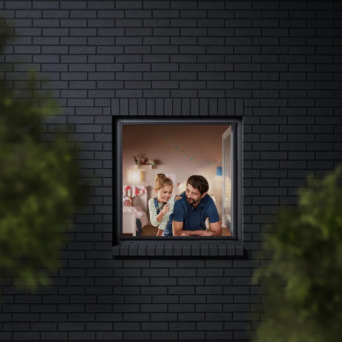 A man and a child are seen through a window, looking into a room decorated with colorful bunting. The building has dark brick walls, and the view is partially framed by blurred greenery. The man is wearing a blue shirt, and the child is sitting beside him. (This text has been generated by AI)