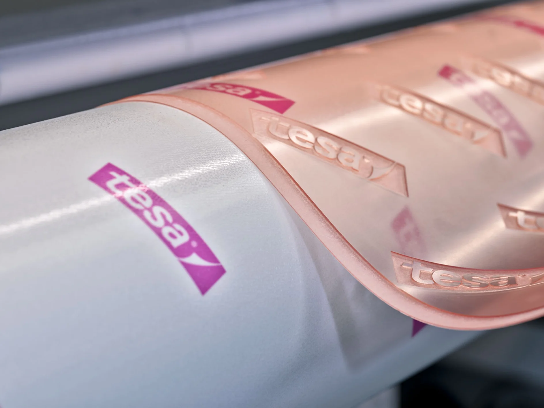 Close-up image of a white cylindrical object partially wrapped with pink transparent tesa tape. The tesa tape and the cylinder have tesa logos printed in white on a pink background. (This text has been generated by AI)