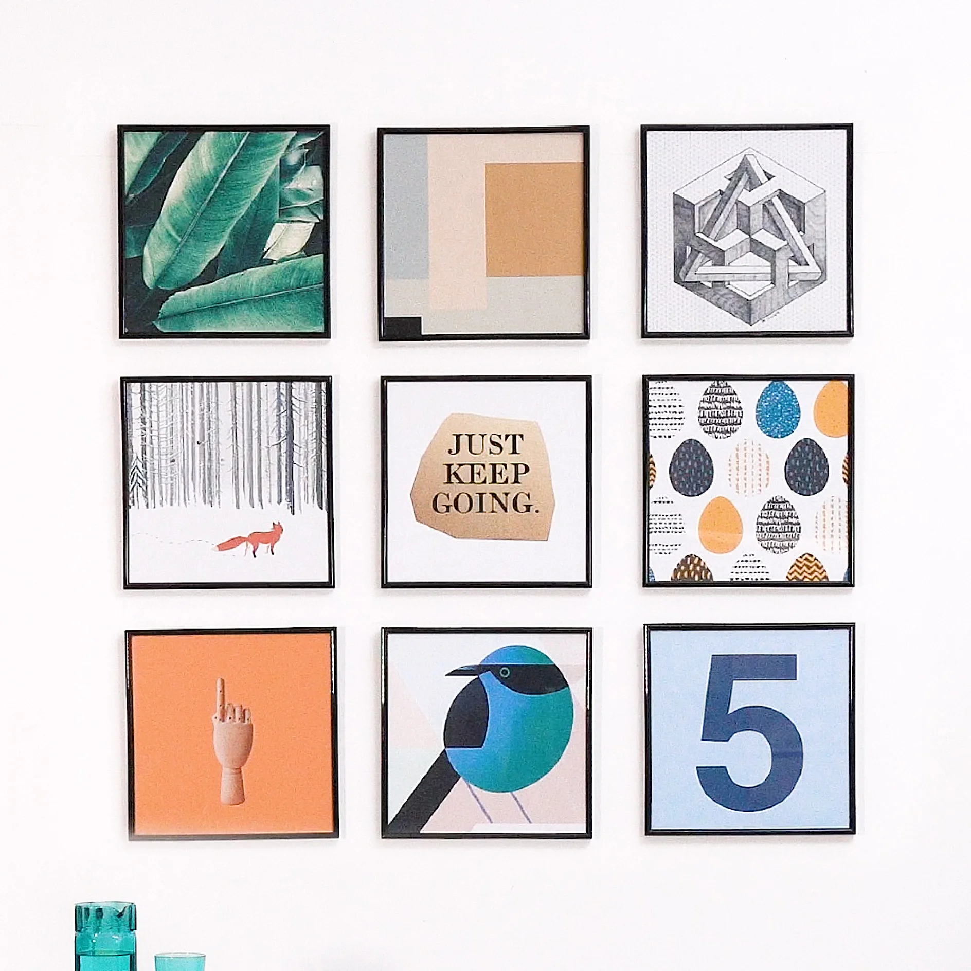 A wall displaying nine framed art pieces. Images include abstract designs, a bird illustration, a large number 5, a forest with a fox, a motivational message Just Keep Going, and a hand pointing upwards, all securely hung using tesa tape. (This text has been generated by AI)