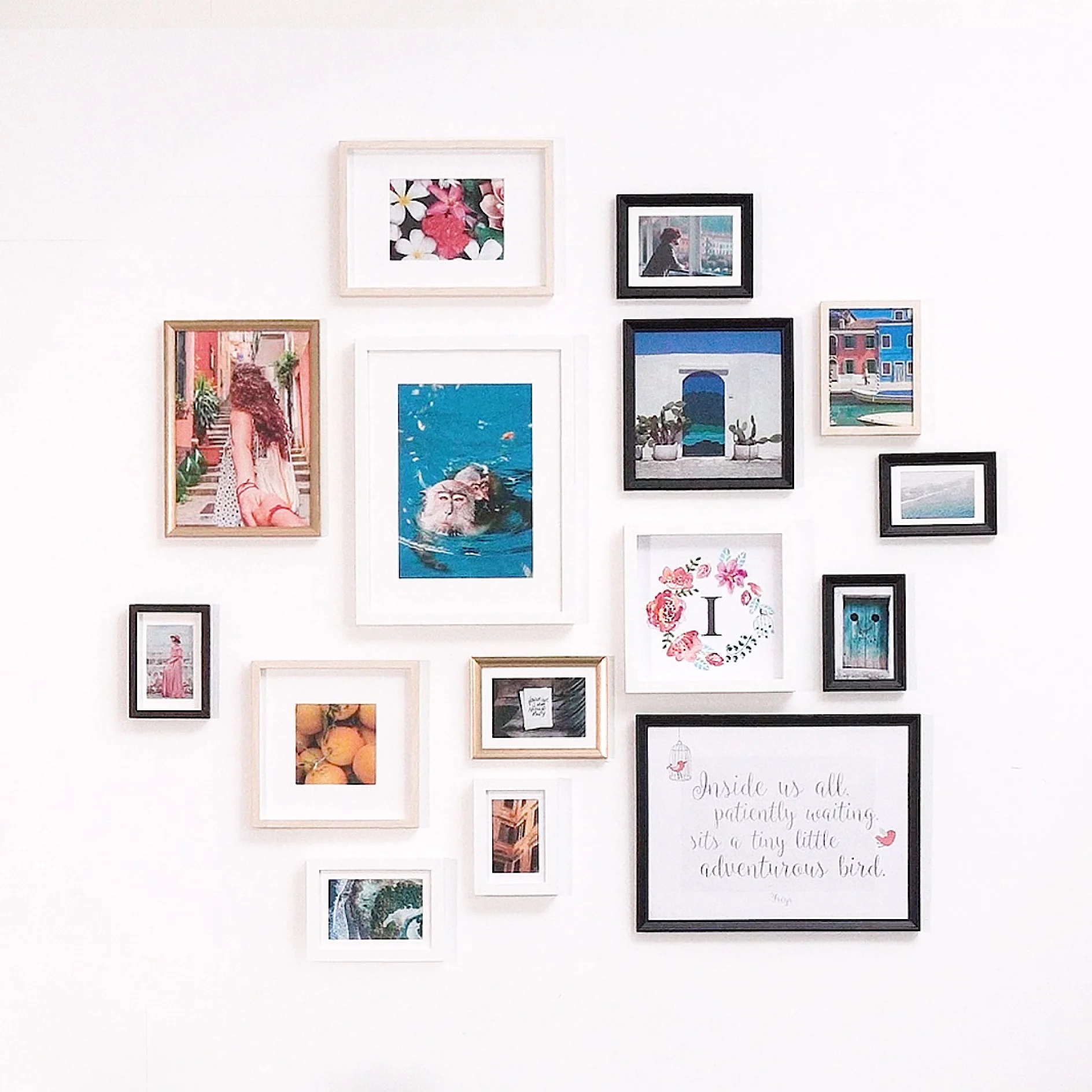 A wall features an arrangement of 15 picture frames in various sizes and colors. The frames display a mix of art, photographs, and text. The collection includes images of a woman, a door, flowers, landscapes, and a framed quote. (This text has been generated by AI)