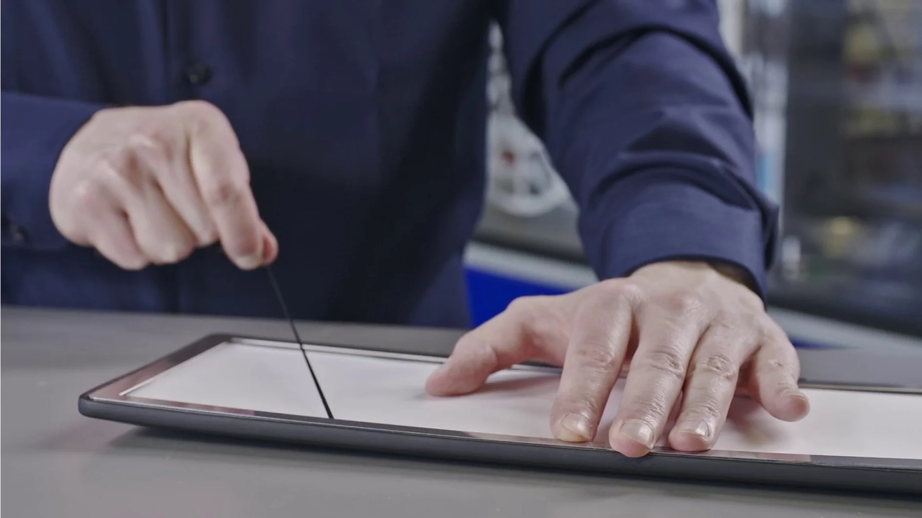 A person in a dark shirt demonstrates the process of resizing a rectangular object using a cutting tool. The person holds the frame with one hand while drawing the tool along the object with tesa tape in the other. (This text has been generated by AI)