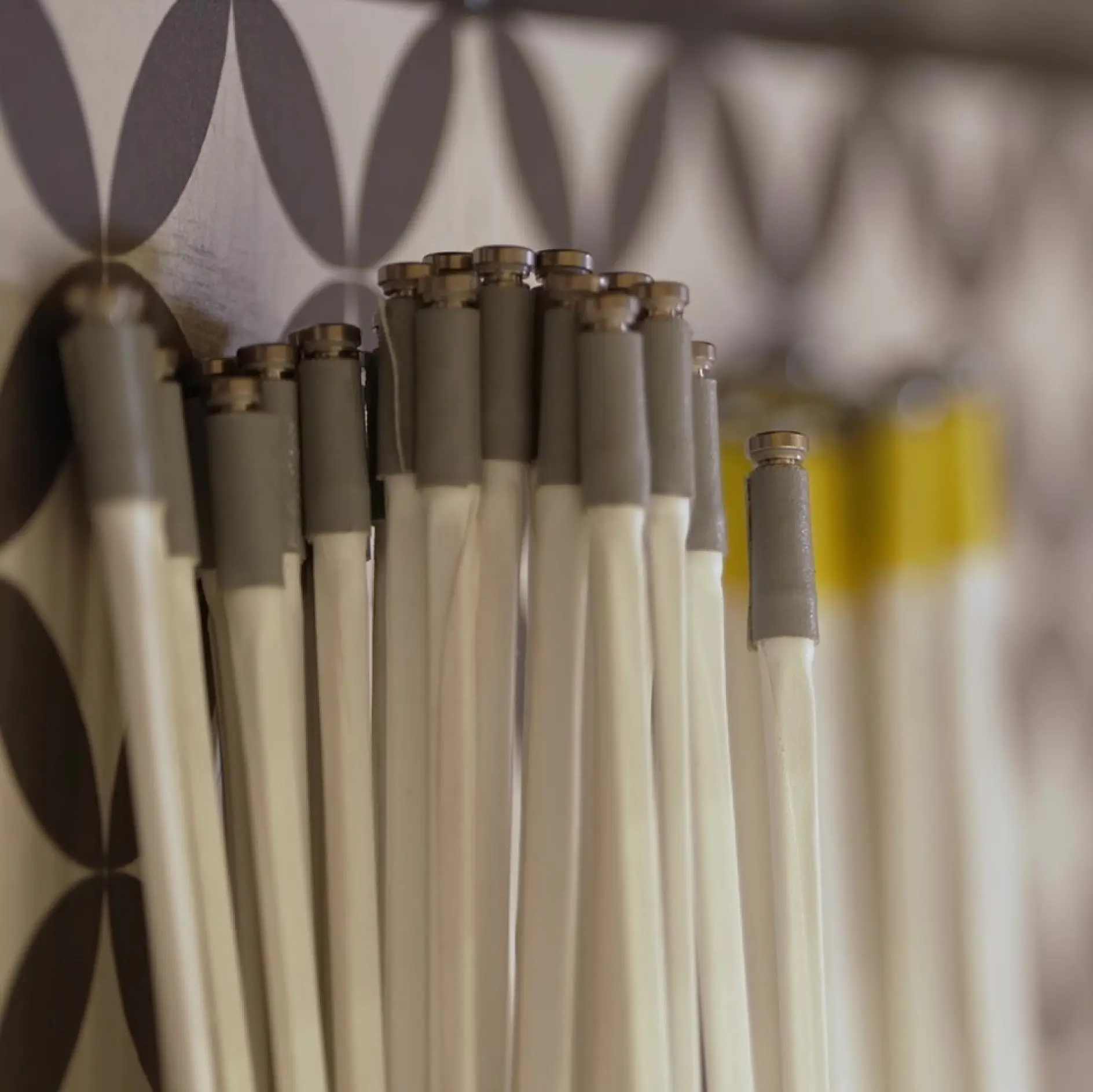 灰色と黄色の持ち手が付いた複数の白い巻き傘のクローズアップ。テサテープでしっかりと巻かれ、模様のある壁に立てかけられています。模様は明るい背景に暗い円形で構成されています。焦点は傘の先端にあります。. (This text has been generated by AI)