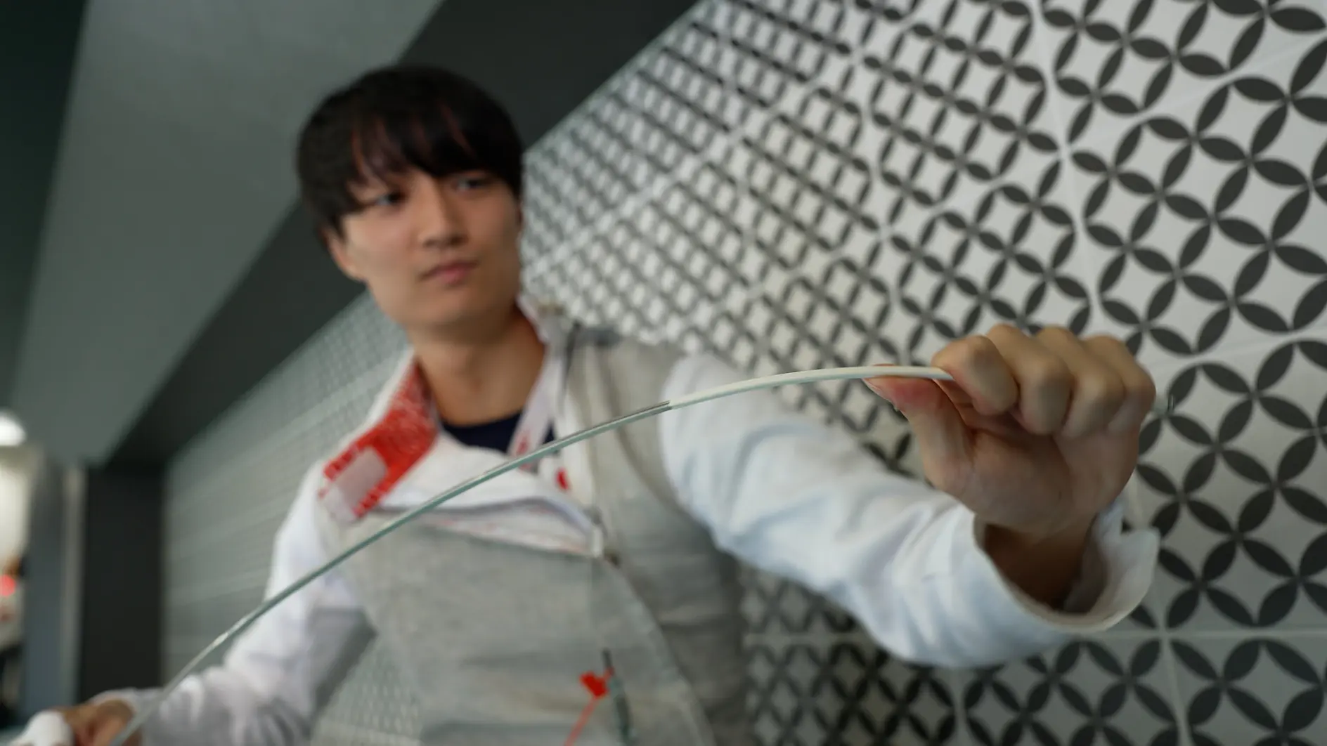 明るい色の服を着た人がフレキシブルケーブルを持ち、それを少し曲げています。背景には、幾何学的な白黒の壁模様があります。この画像は、テサテープを使用しながらケーブルを曲げる動作に焦点を当てています。.