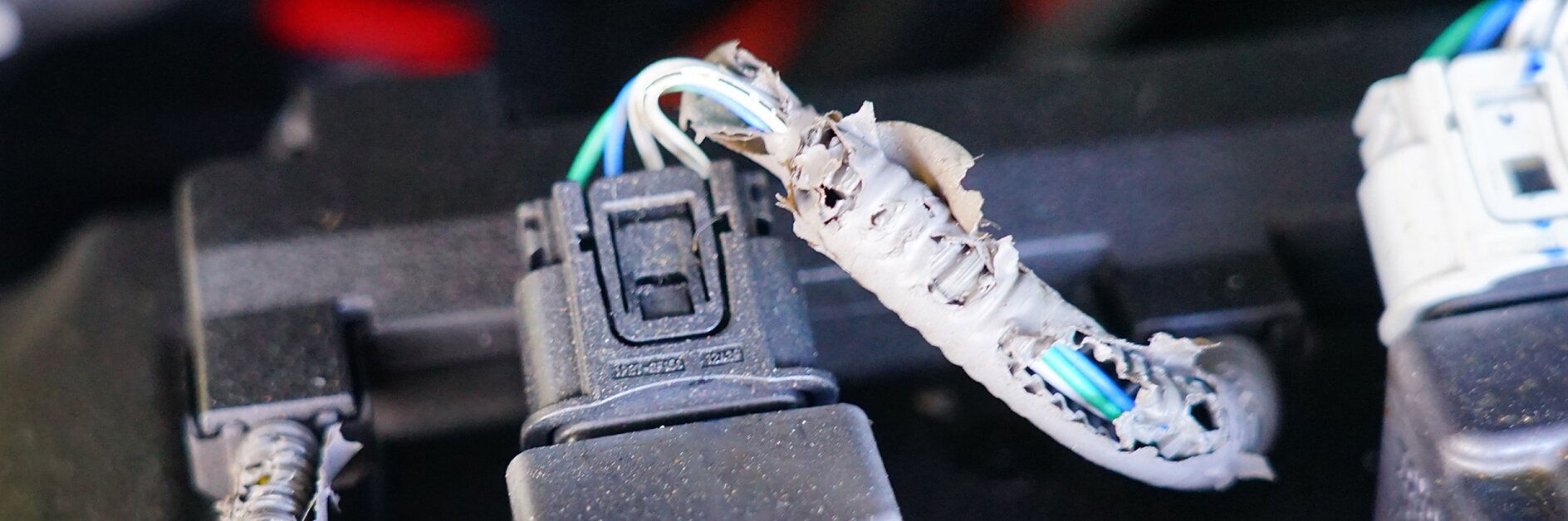 Three electrical connectors with visible damage to the insulation, exposing wires. The insulation appears chewed or torn, showing multiple colored wires inside. The connectors are attached to a black base and wrapped with tesa tape for added protection. (This text has been generated by AI)