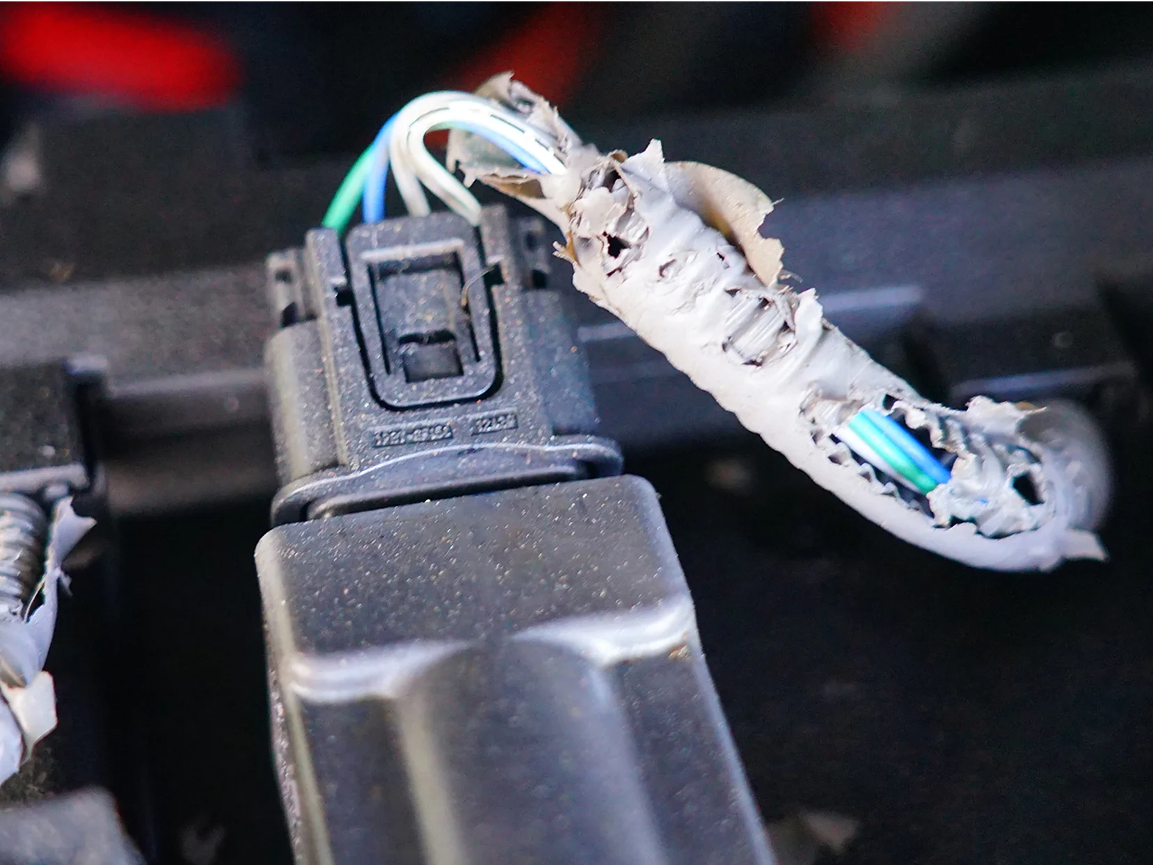 Three electrical connectors with visible damage to the insulation, exposing wires. The insulation appears chewed or torn, showing multiple colored wires inside. The connectors are attached to a black base and wrapped with tesa tape for added protection. (This text has been generated by AI)