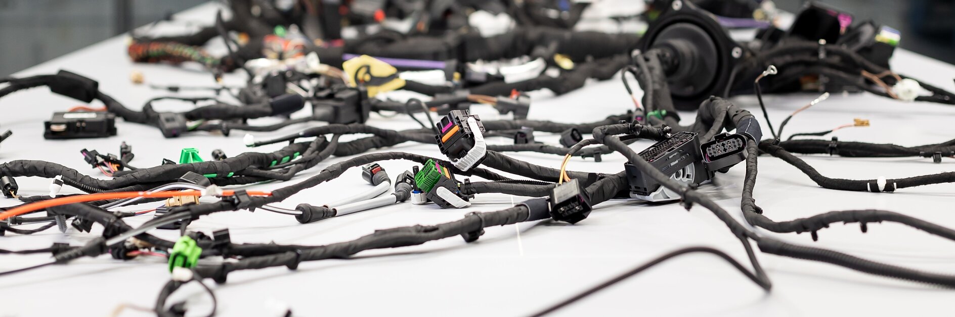 A large number of electronic cables and connectors are spread across a white table. The background shows blurred glass windows and a building exterior. The setup appears to be in a work or testing area for electronics, where tesa tape is likely used to secure or organize the cables effectively. (This text has been generated by AI)