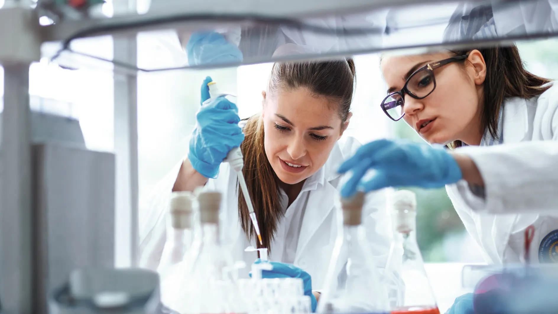 scientists wearing lab coats and blue gloves handling glassware in a laboratory setting with chemical equipment visible