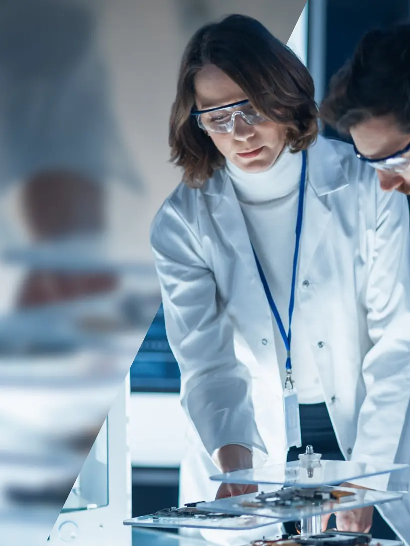 Two scientists wearing white lab coats and safety goggles work together in a laboratory. They examine a piece of equipment held together by tesa tape on a table surrounded by various scientific apparatus. The setting is modern and well-lit. (This text has been generated by AI)