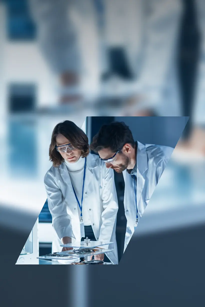 Two scientists wearing lab coats and safety goggles are working in a laboratory. They are standing over a table, examining equipment or samples. The scene is framed within a triangle on a blurred background, prominently featuring tesa tape used in their experiments. (This text has been generated by AI)