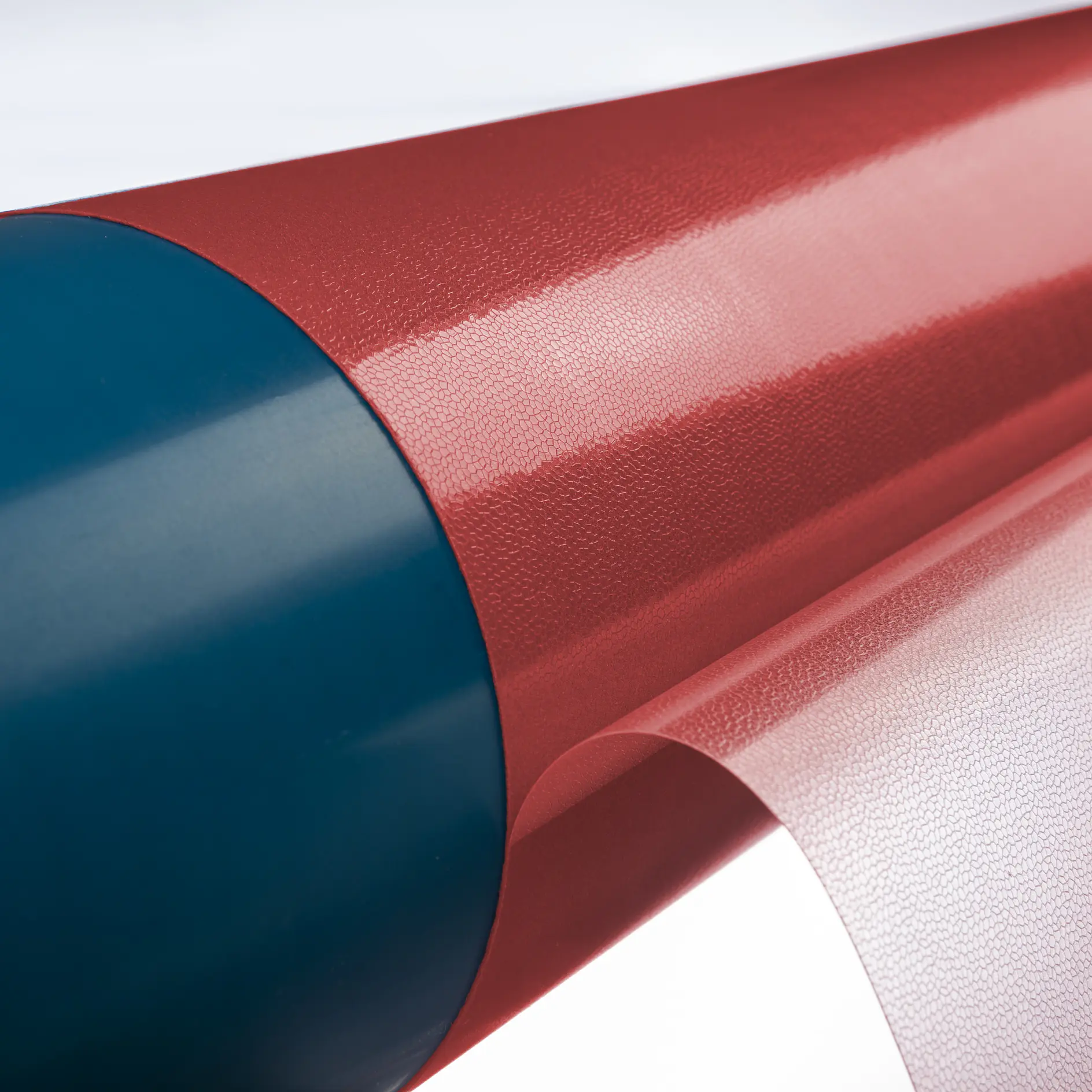 A close-up of a roll of textured red material with a smooth, translucent sheet being unrolled from it. The cylinder core is dark blue. The surface shows a subtle grid-like pattern on the tesa tape.