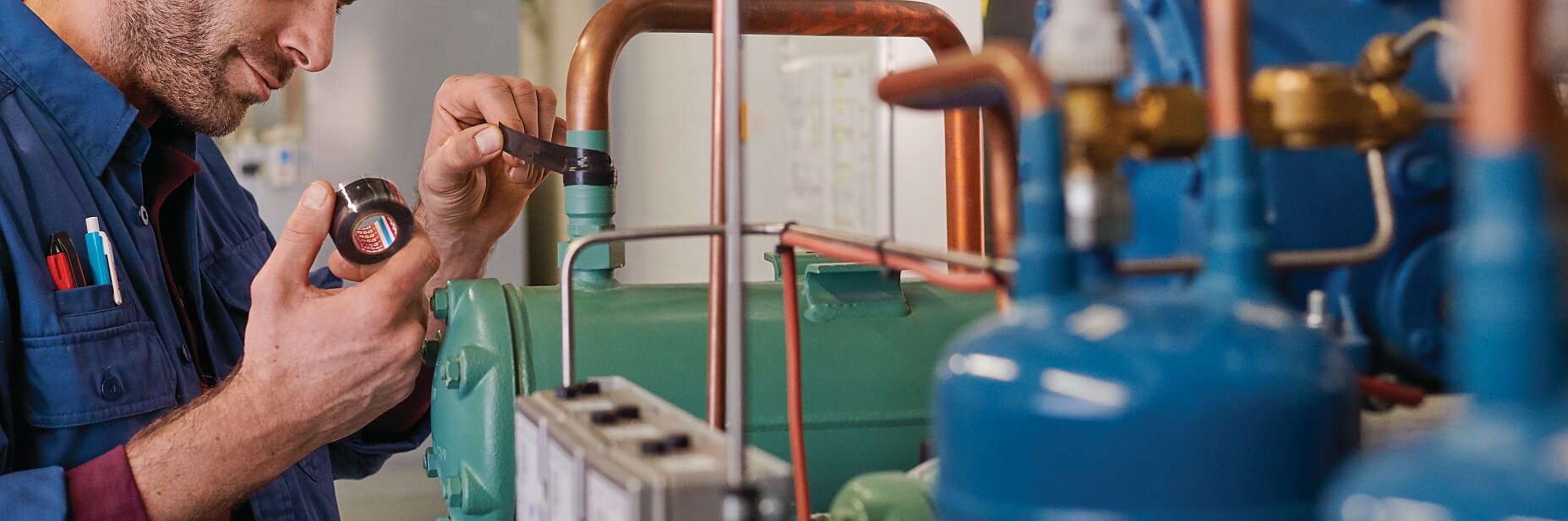 technician in blue uniform inspecting industrial pipes and gauges indoors, focusing on maintenance and system checks