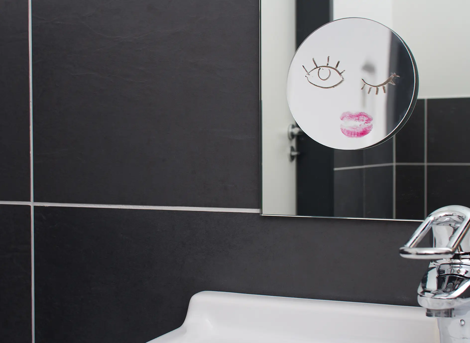 Ant sienos pakabintas vonios veidrodis, prie kurio priklijuotas mažesnis makiažo veidrodis.