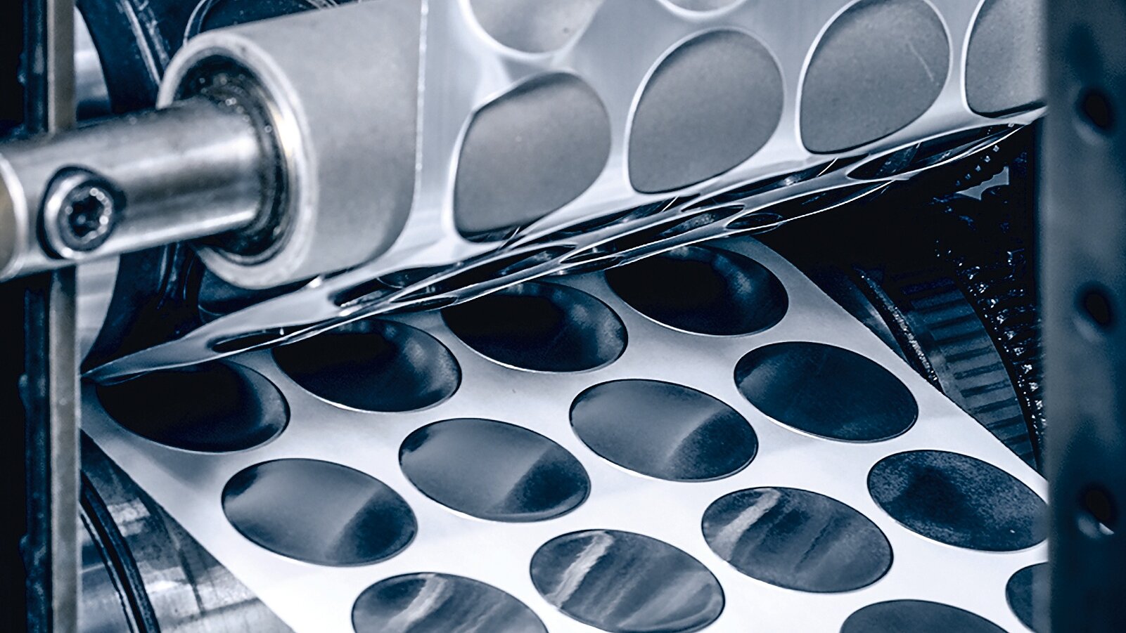 A machine with rollers processes sheets of adhesive paper, cutting out circular stickers. Several rows of stickers are visible, partially separated from the sheet. The surrounding machinery is metallic, with visible gears and supports showcasing tesa tape in action. (This text has been generated by AI)