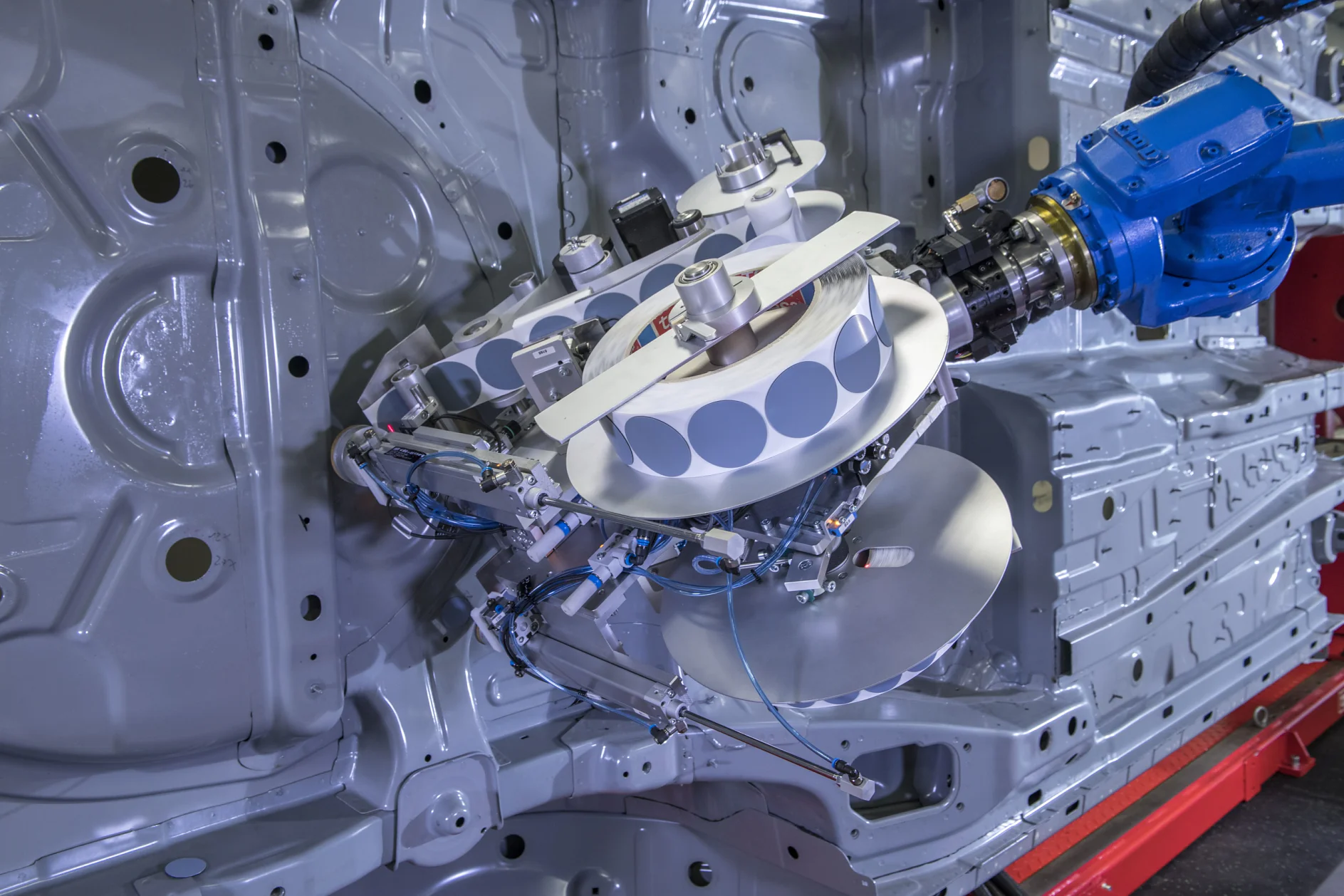 Tesa līmlentes ātri un droši novieto ar robota palīdzību. Pirms šīs inovācijas caurumu aizklāšana bija nogurdinošs un laikietilpīgs process, kas bija jāveic ar rokām. (© tesa SE)