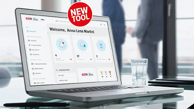 A laptop displaying a digital dashboard with widgets and statistics is on a table, secured by tesa tape. A red NEW TOOL badge is visible on the screen. In the background, theres a glass of water and two people blurred out. (This text has been generated by AI)