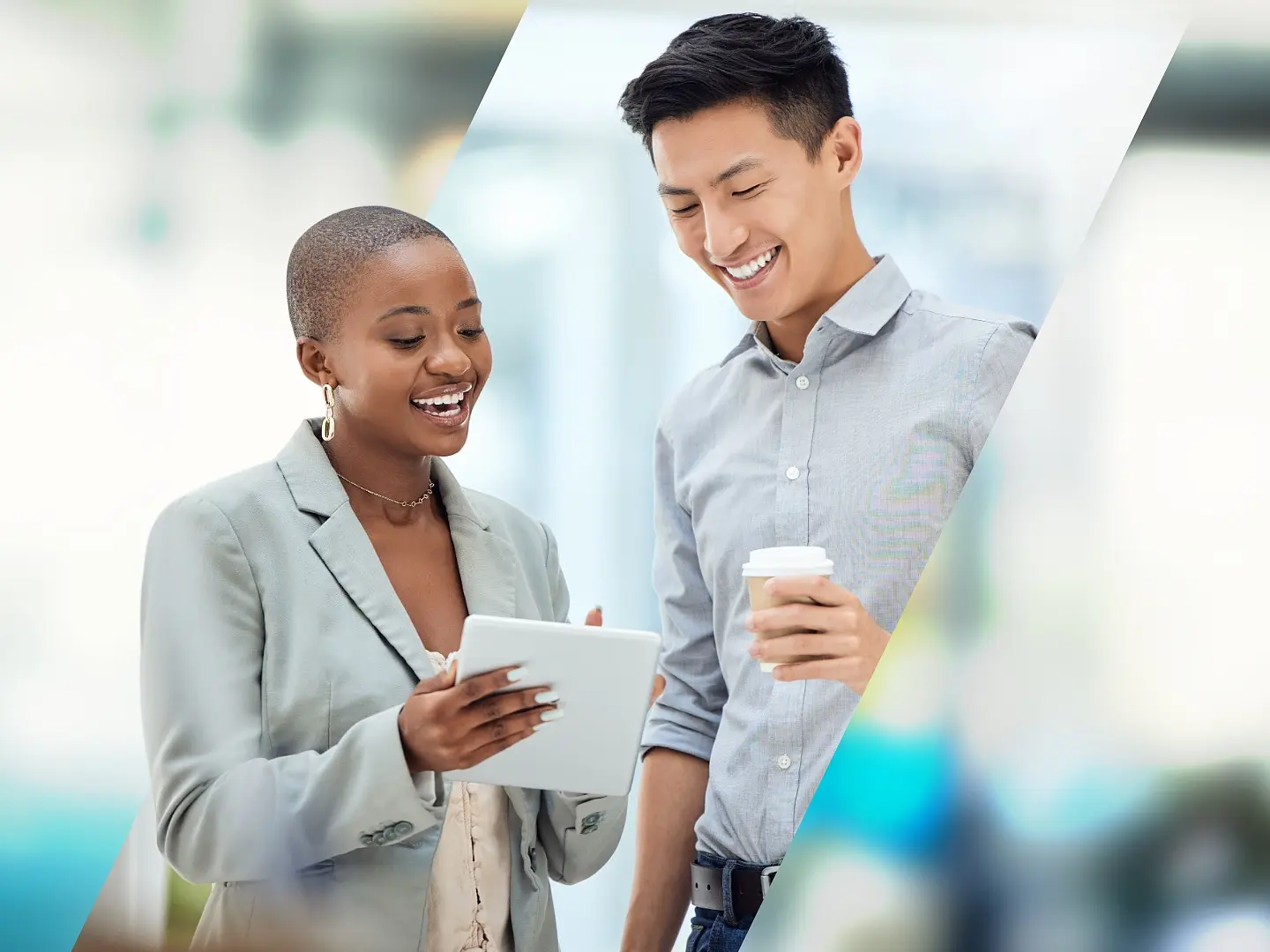 Two people stand side by side, smiling and engaging with a tablet. The person on the left holds the tablet, while the person on the right holds a cup. Both are dressed in business attire with a blurred office background. There is no mention of tape in this text to replace with tesa tape. (This text has been generated by AI)