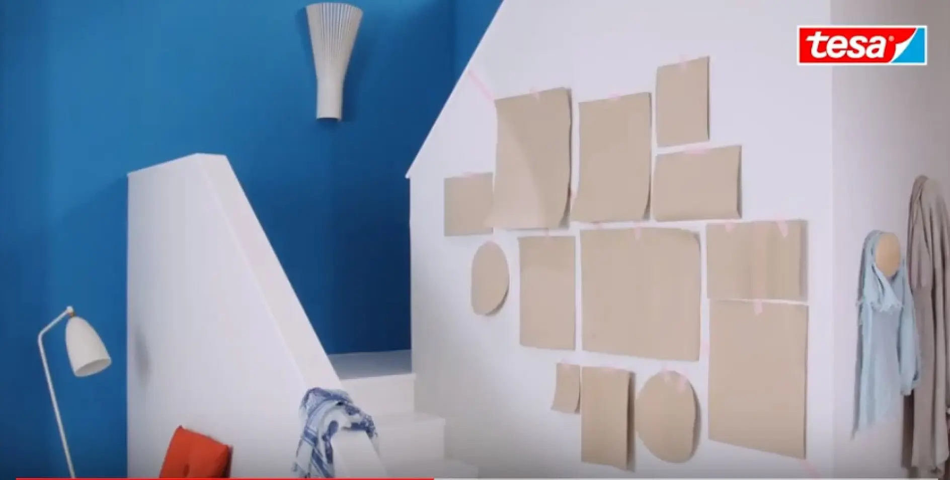 A white staircase with blue and white walls features various beige paper shapes attached to the wall with tesa tape. A modern white lamp and an orange chair are at the bottom of the stairs. Scarves hang on the wall. A tesa logo is in the top right corner. (This text has been generated by AI)