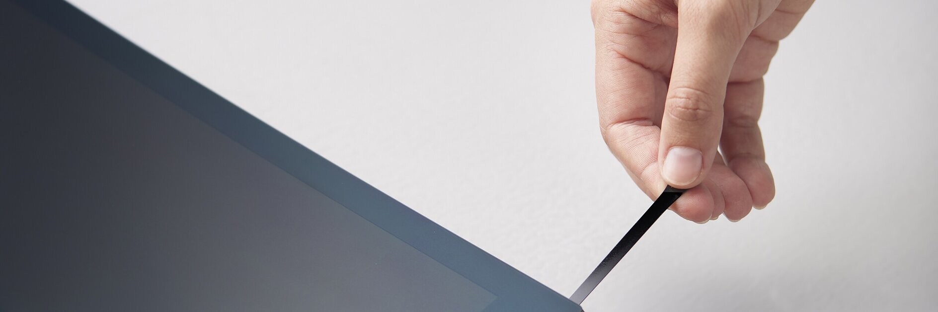 hand pulling black tesa strip from edge of laptop screen in a bright indoor setting