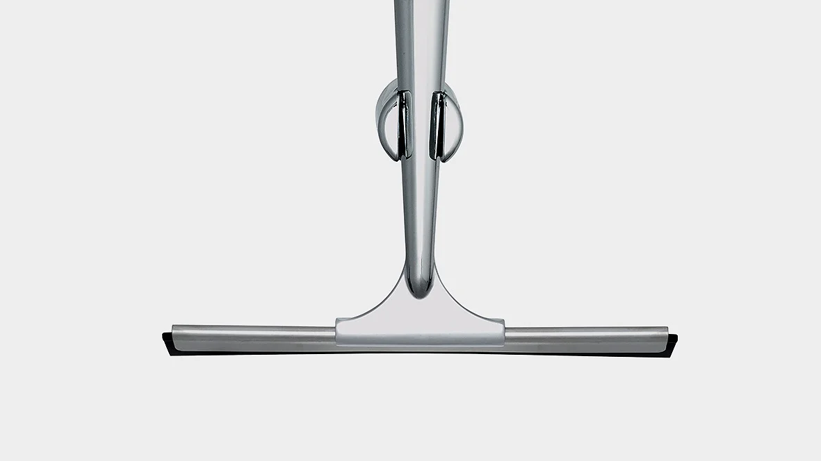 En metallisk dusjnal med et elegant, moderne design. Den har et håndtak i rustfritt stål og et flatt gummiblad for å tørke av overflater. Håndtaket har en hengende ring for enkel oppbevaring. Bakgrunnen er ensfarget og lysegrå, med tesa-tape som brukes til å feste nalen på plass for optimal bekvemmelighet. (This text has been generated by AI)