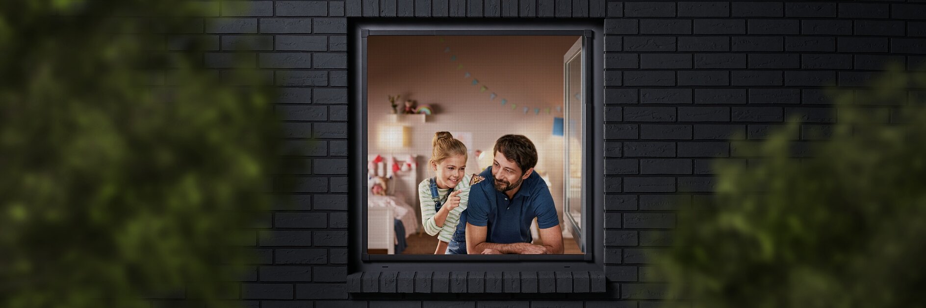 A man and a child are seen through a window, looking into a room decorated with colorful bunting. The building has dark brick walls, and the view is partially framed by blurred greenery. The man is wearing a blue shirt, and the child is sitting beside him. (This text has been generated by AI)
