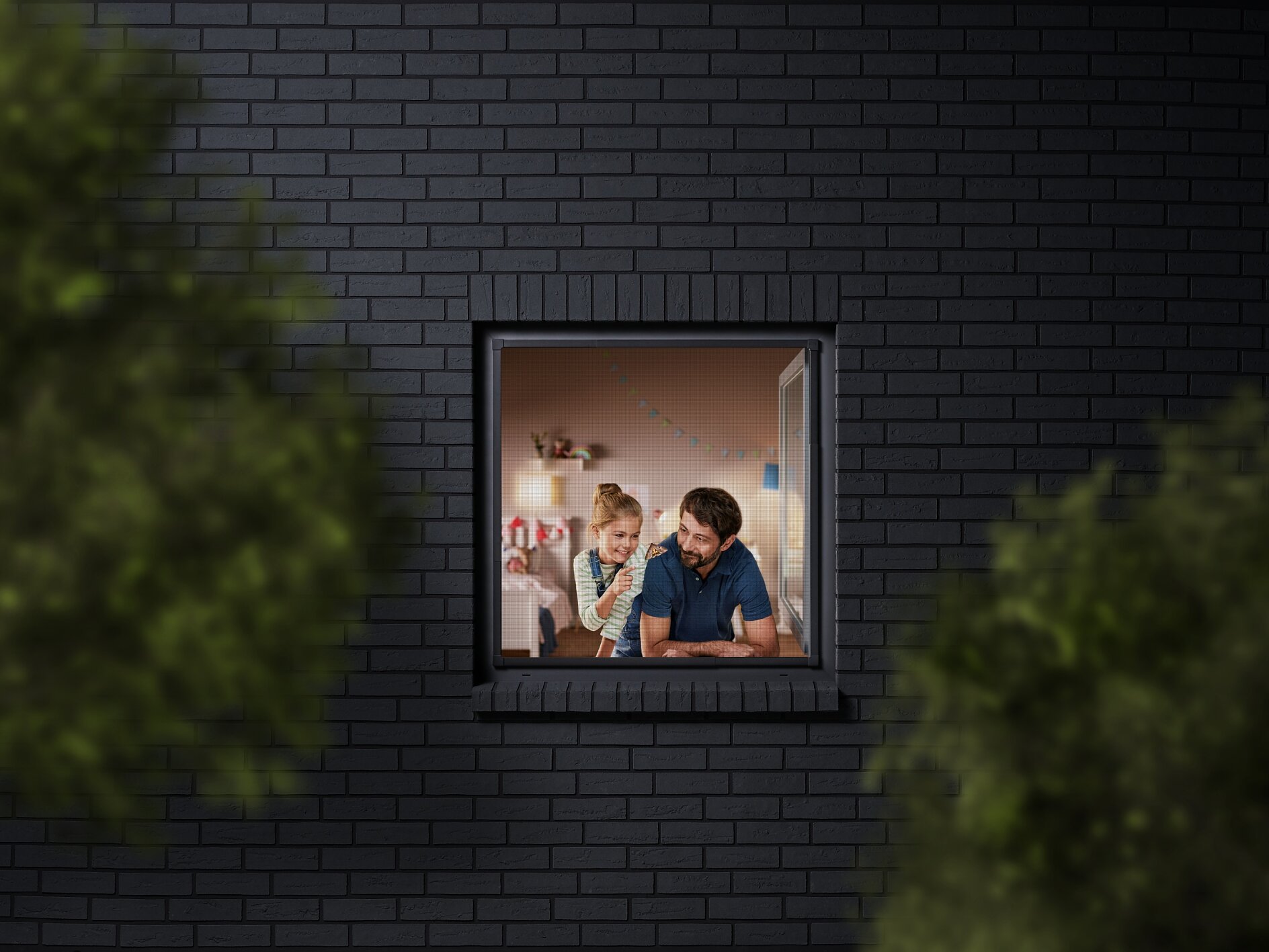A man and a child are seen through a window, looking into a room decorated with colorful bunting. The building has dark brick walls, and the view is partially framed by blurred greenery. The man is wearing a blue shirt, and the child is sitting beside him. (This text has been generated by AI)