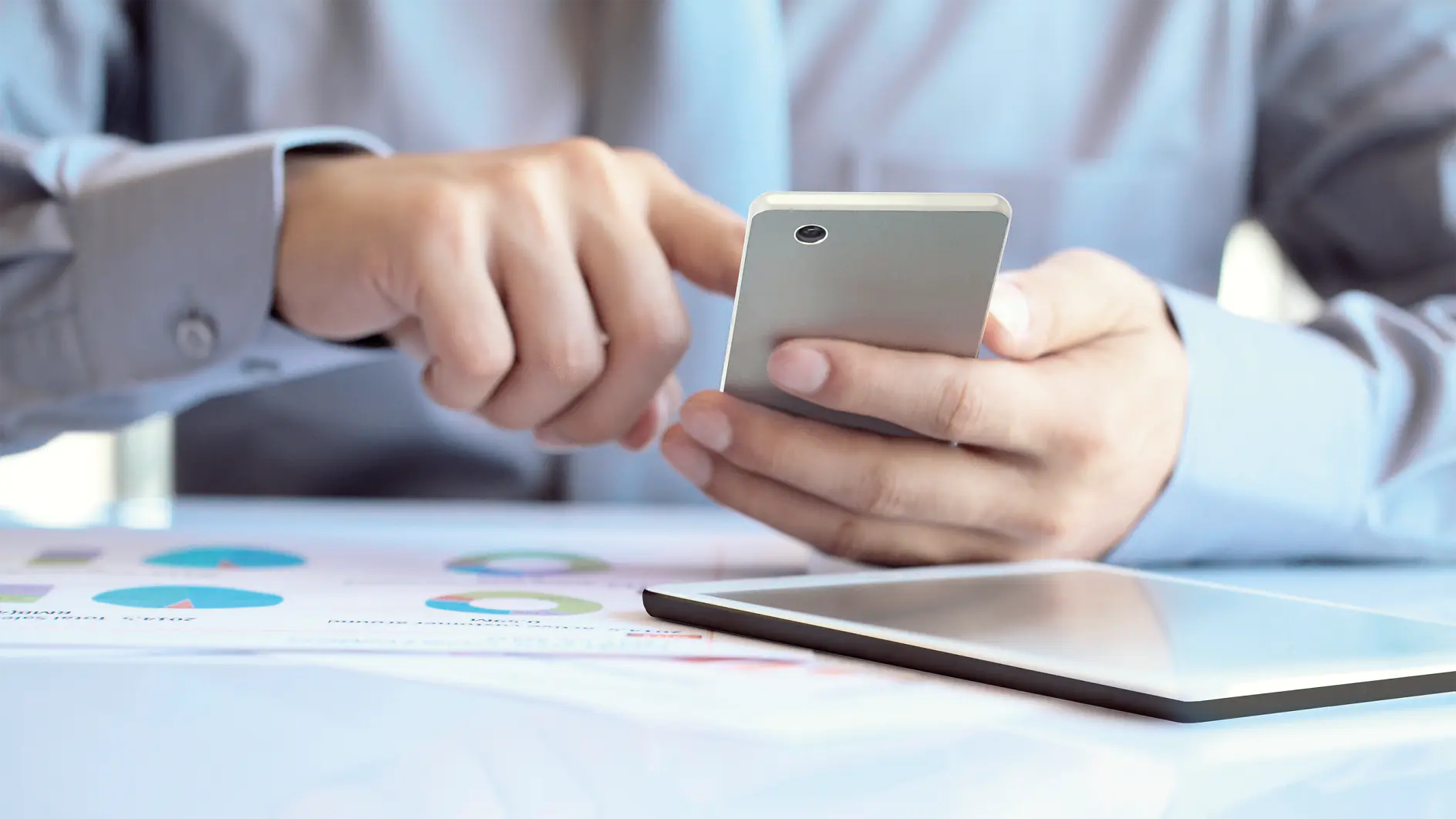 tesa-man-gebruikt-smartphone-met-tablet-en-grafieken