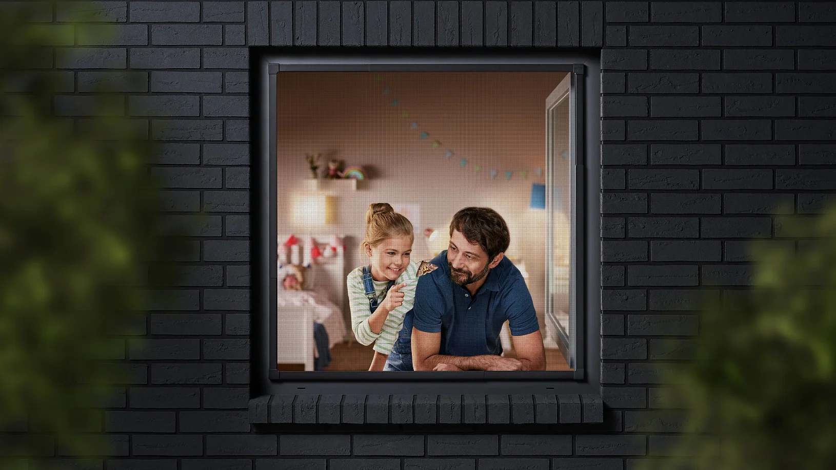 A man and a child are seen through a window, looking into a room decorated with colorful bunting. The building has dark brick walls, and the view is partially framed by blurred greenery. The man is wearing a blue shirt, and the child is sitting beside him. (This text has been generated by AI)