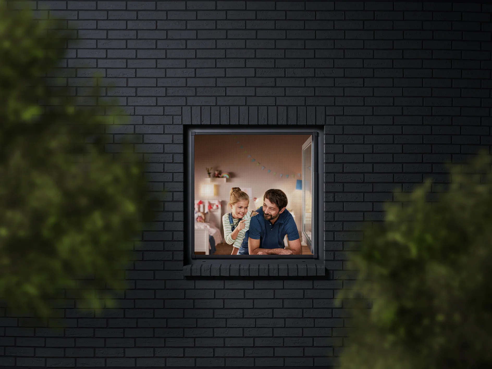 A man and a child are seen through a window, looking into a room decorated with colorful bunting. The building has dark brick walls, and the view is partially framed by blurred greenery. The man is wearing a blue shirt, and the child is sitting beside him. (This text has been generated by AI)