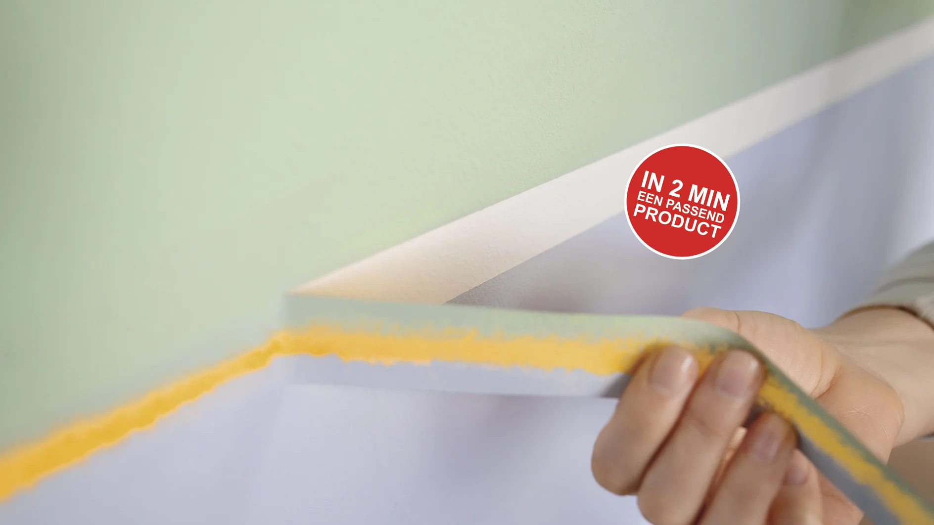 Een hand trekt een strook witte tesa-tape van een muur, waardoor een strakke lijn tussen lichtgroene en witte verf zichtbaar wordt. Er zit een rode ronde sticker op de muur met de tekst: IN 2 MIN EER PASSENDE PRODUCT. (This text has been generated by AI)