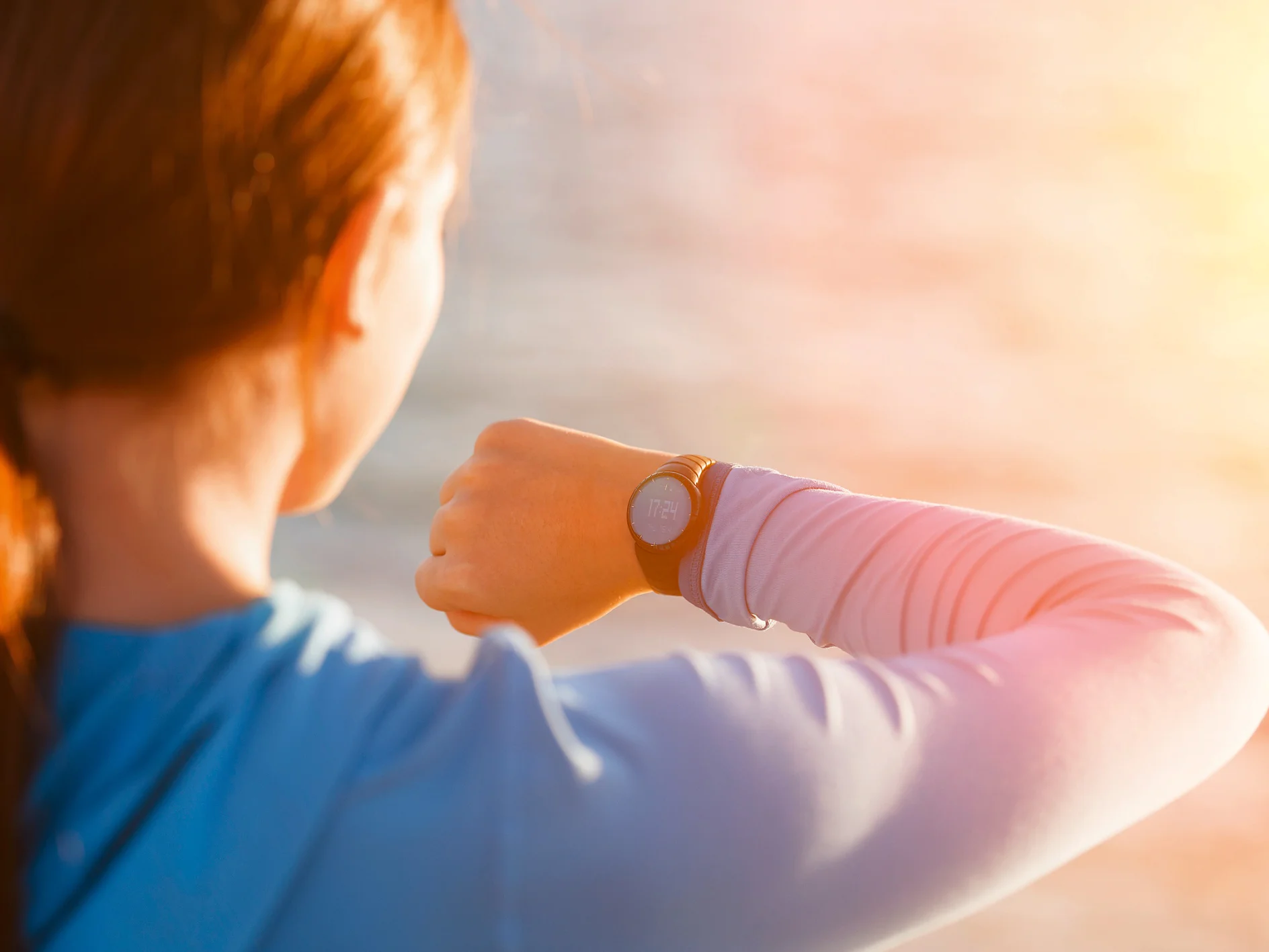 vrouw in blauw shirt buiten kijkt op smartwatch om de tijd te controleren met zonlicht op de achtergrond tesa (This text has been generated by AI)