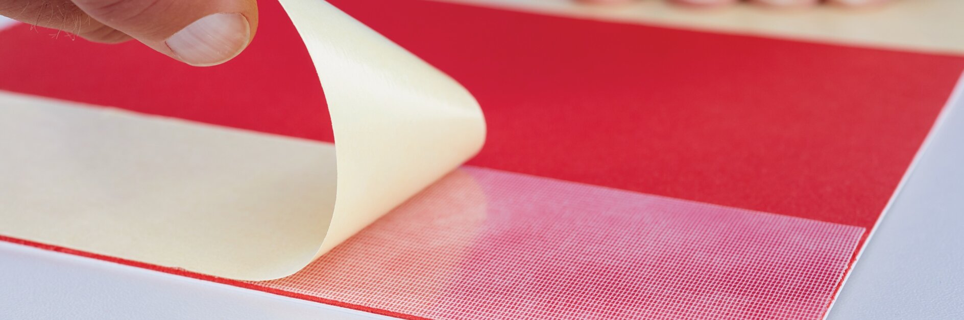 hand peeling red tesa tape backing on white surface with blurred hand in background
