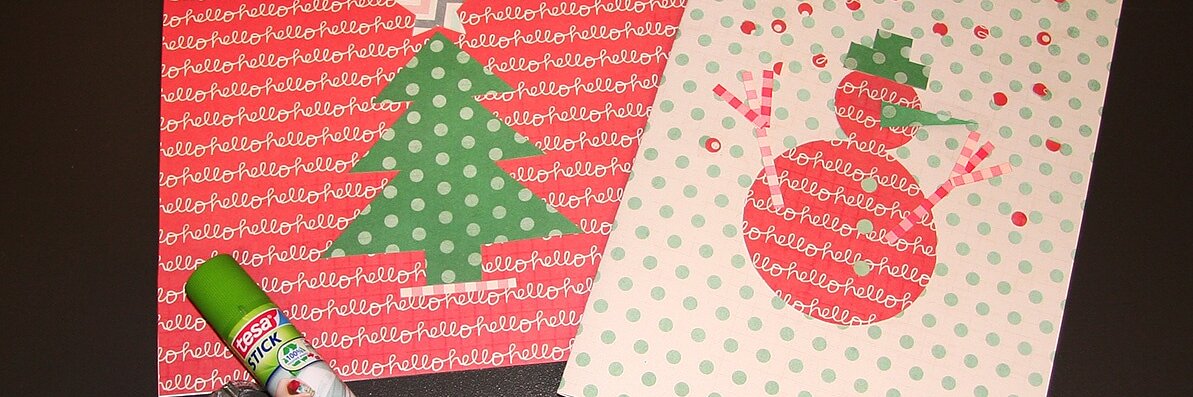 Dwie ręcznie robione kartki leżą na ciemnej powierzchni. Lewa kartka przedstawia zieloną choinkę na czerwonym papierze z tekstem „hello”. Prawa kartka przedstawia bałwana na zielonym papierze w kropki. Obok nich znajduje się klej w sztyfcie i dozownik taśmy tesa. (This text has been generated by AI)