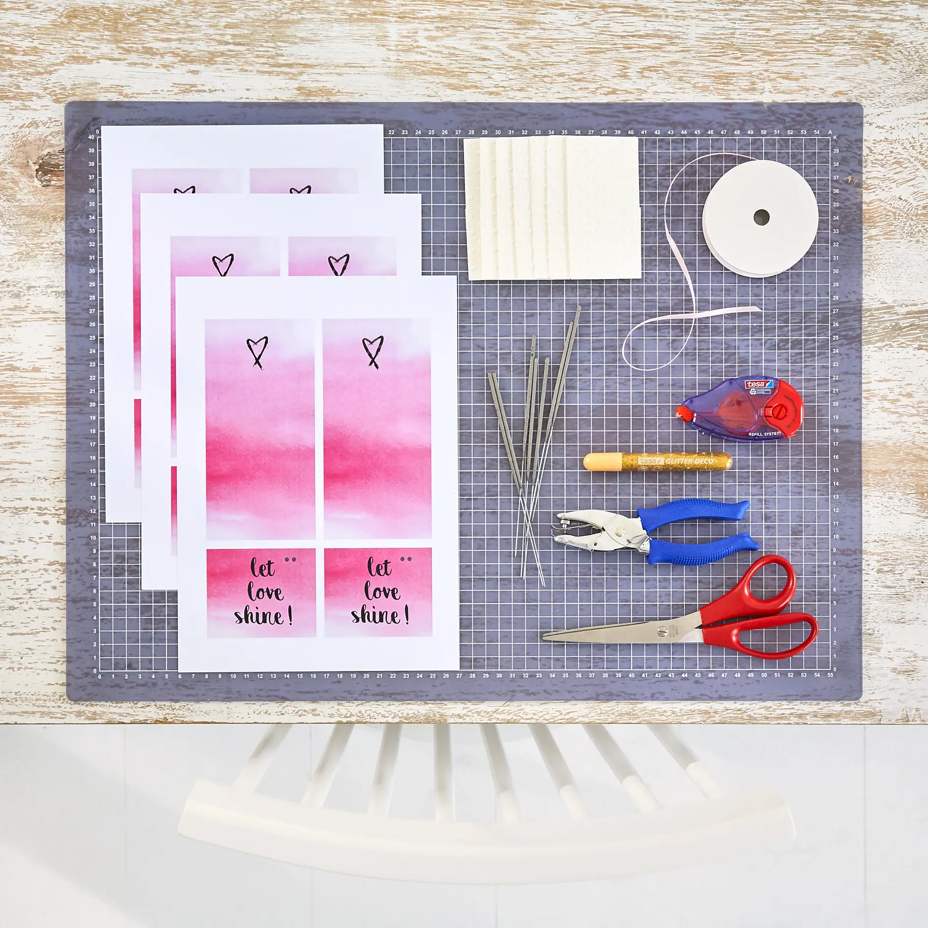 szablony wydrukowane na sztywnym papierze, satynowa wstążka w różowym odcieniu (o szerokości 3 mm), szczypce do dziurkowania, nożyczki, chusteczki z tłoczonego papieru, zimne ognie, klej w taśmie tesa ecoLogo®, klej z brokatem tesa®